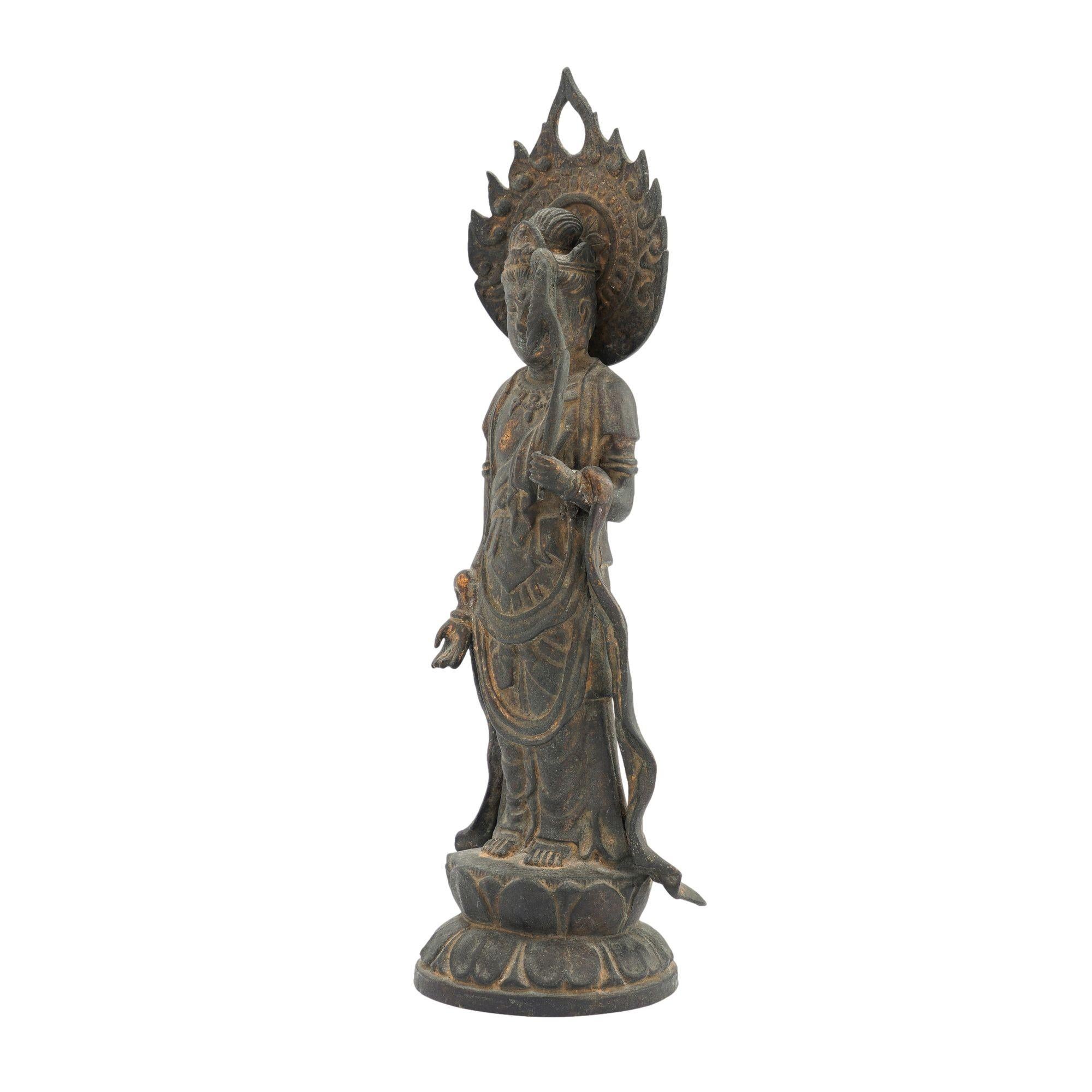 Cast bronze statue of a half draped figure of the standing Bodhisattva on a lotus plinth, with a removable flaming nimbus surrounding the head. The figure holds a lotus, the symbol of purity and worldly detachment, in their raised left hand, with