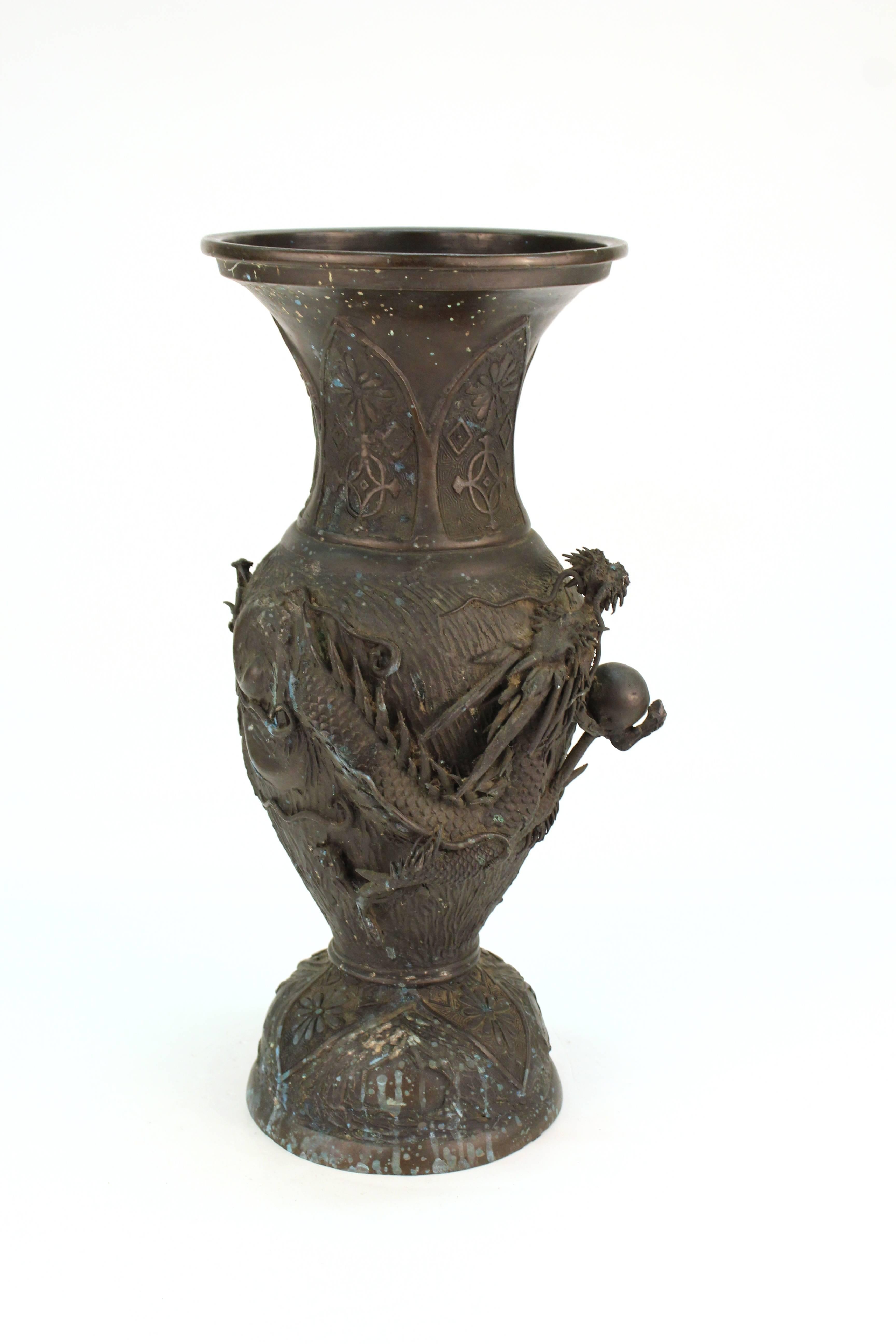 A sculpted Japanese vase in cast metal, with a dragon theme sculpted on the outer circumference. The piece has color splatter on one side and is in good vintage condition.