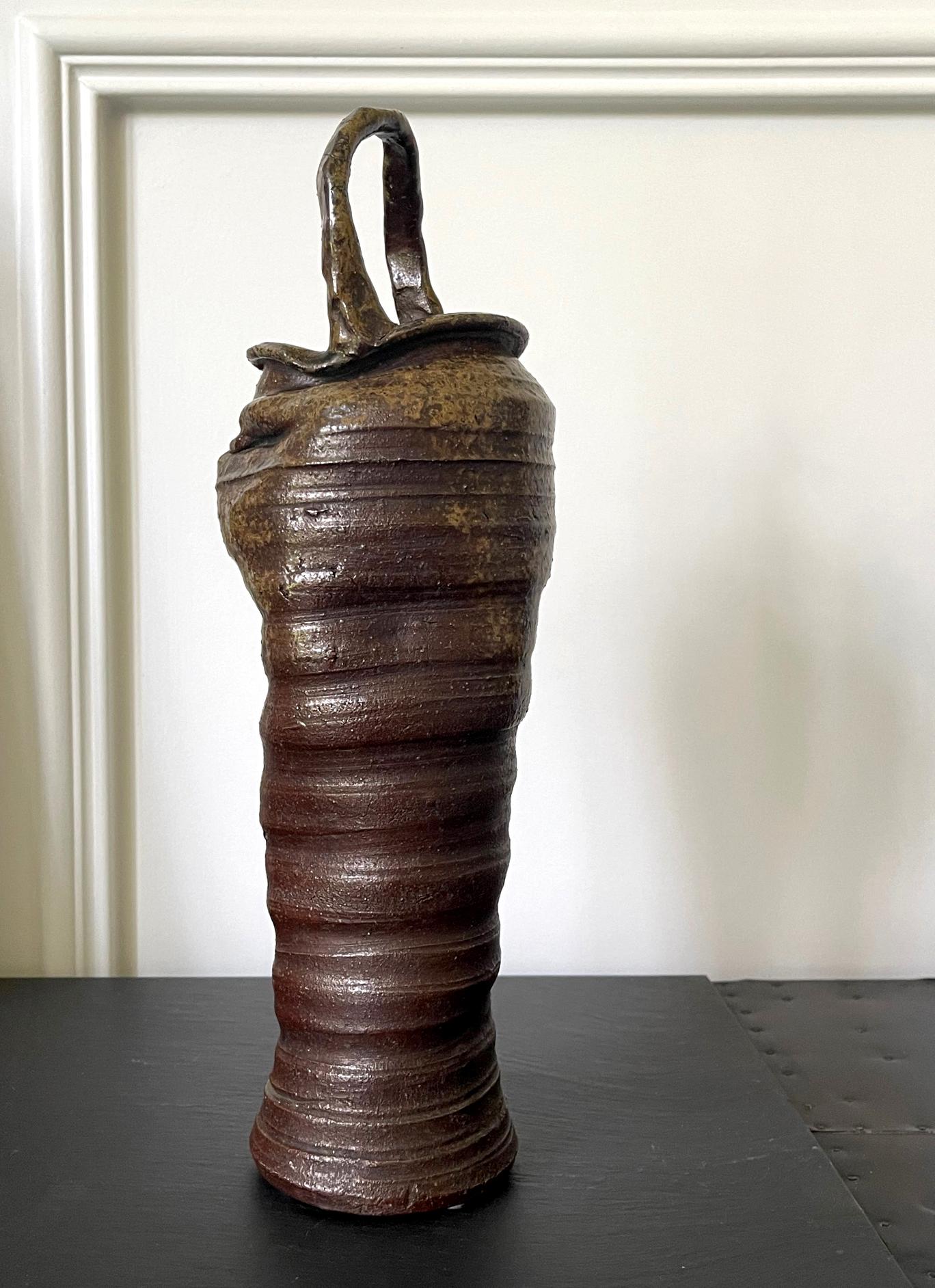 A tall vintage ceramic vase with handle from Japan (20th century) by Nanba Koyo. Made in the tradition of Bizen ware, the vase has a modern aesthetic with a slender and elegant upright form. Intentional potted rings circumvent much of its irregular