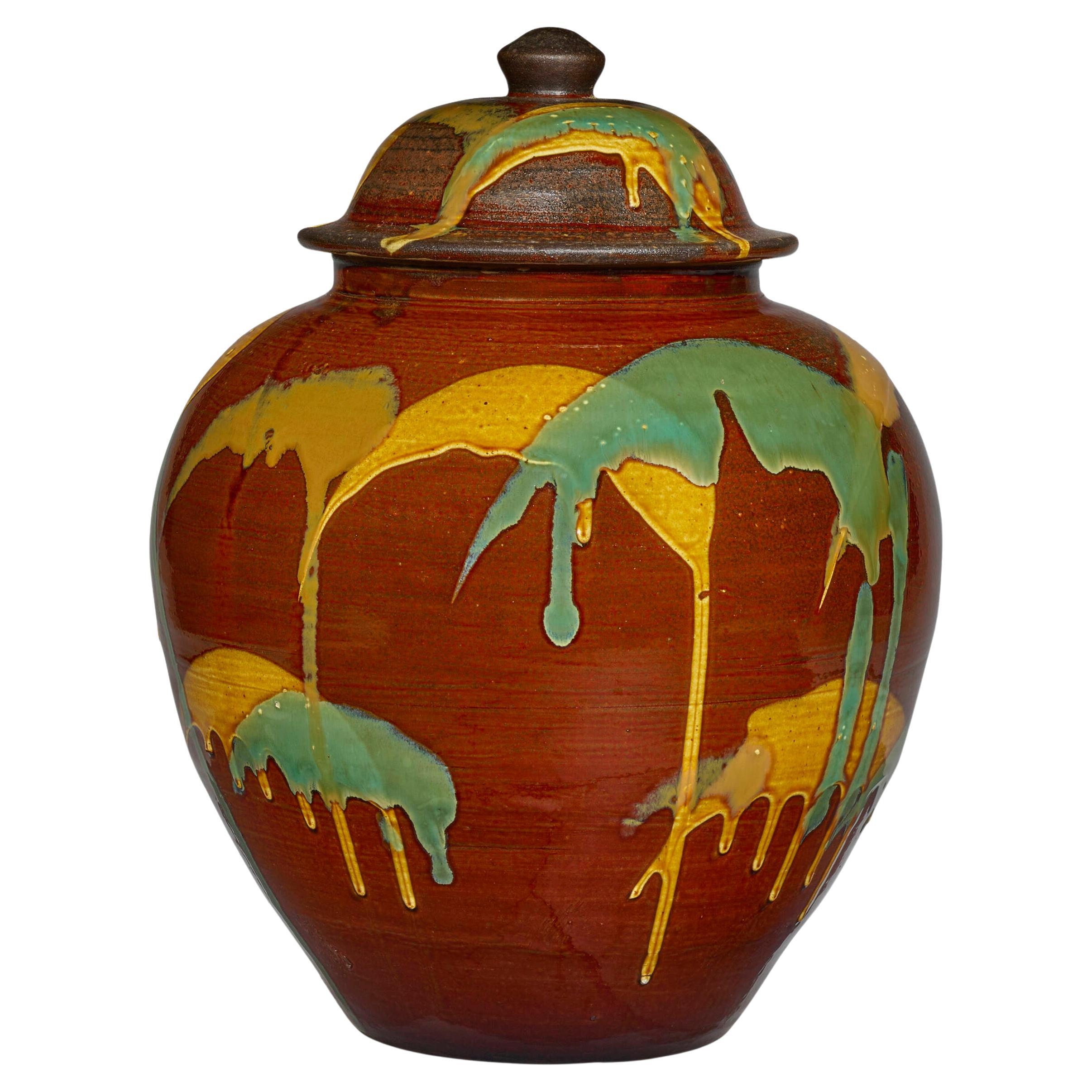 A Japanese lidded ceramic jar from the kiln of Onda Yaki, circa 2007. The stoneware jar impresses the viewer with a robust bulbous form. and exuberantly splashed and dripped glaze in yellow and green on a contrasting ocher background. The visual