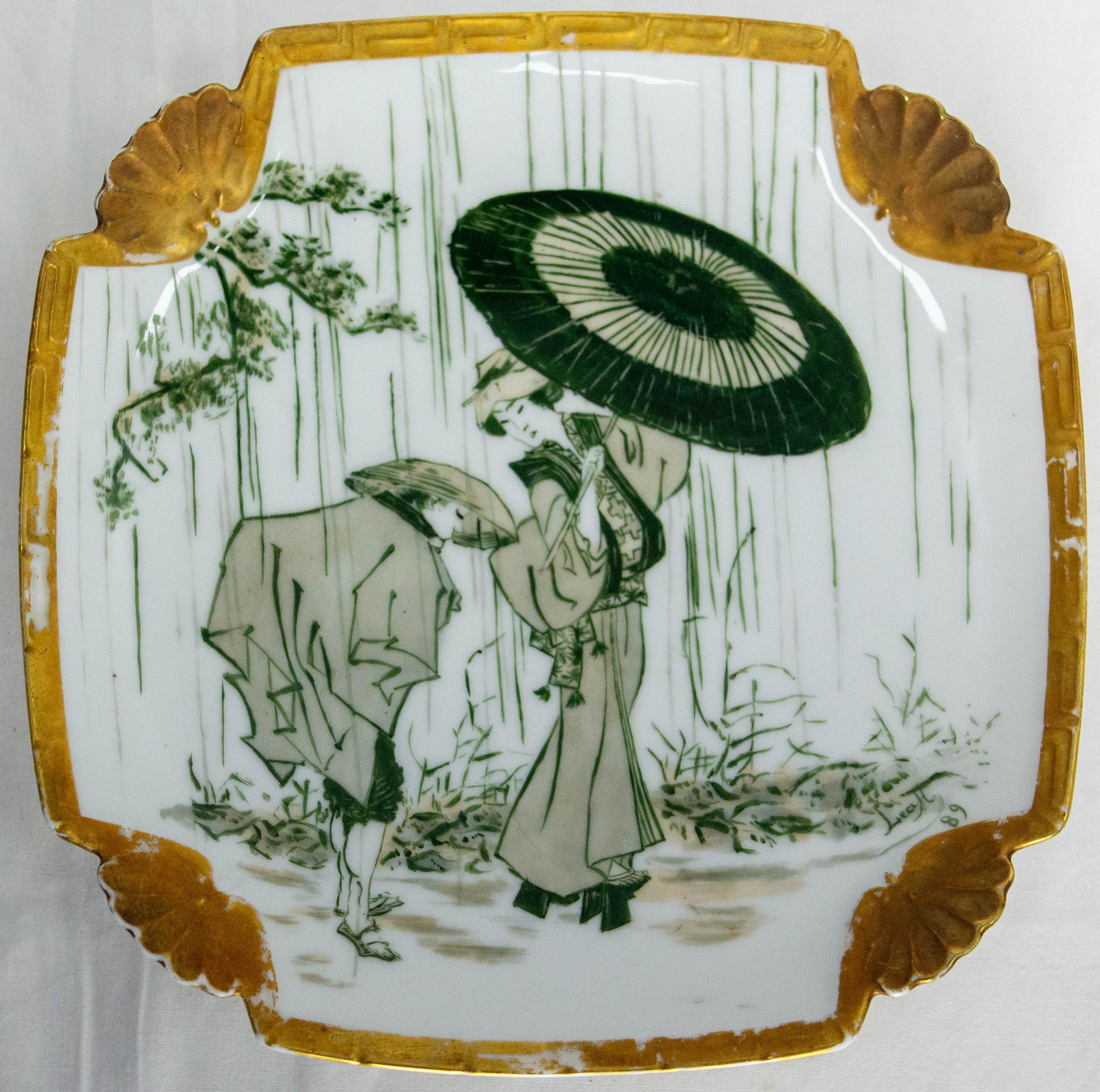 Ein quadratischer Teller im japanischen Stil, der typisch ist für die Verliebtheit Europas in östliche Kulturen im 19.
Keramik mit einer Geisha, die im Regen einen Regenschirm trägt, und blühenden Kirschzweigen.
Hergestellt um das 19.