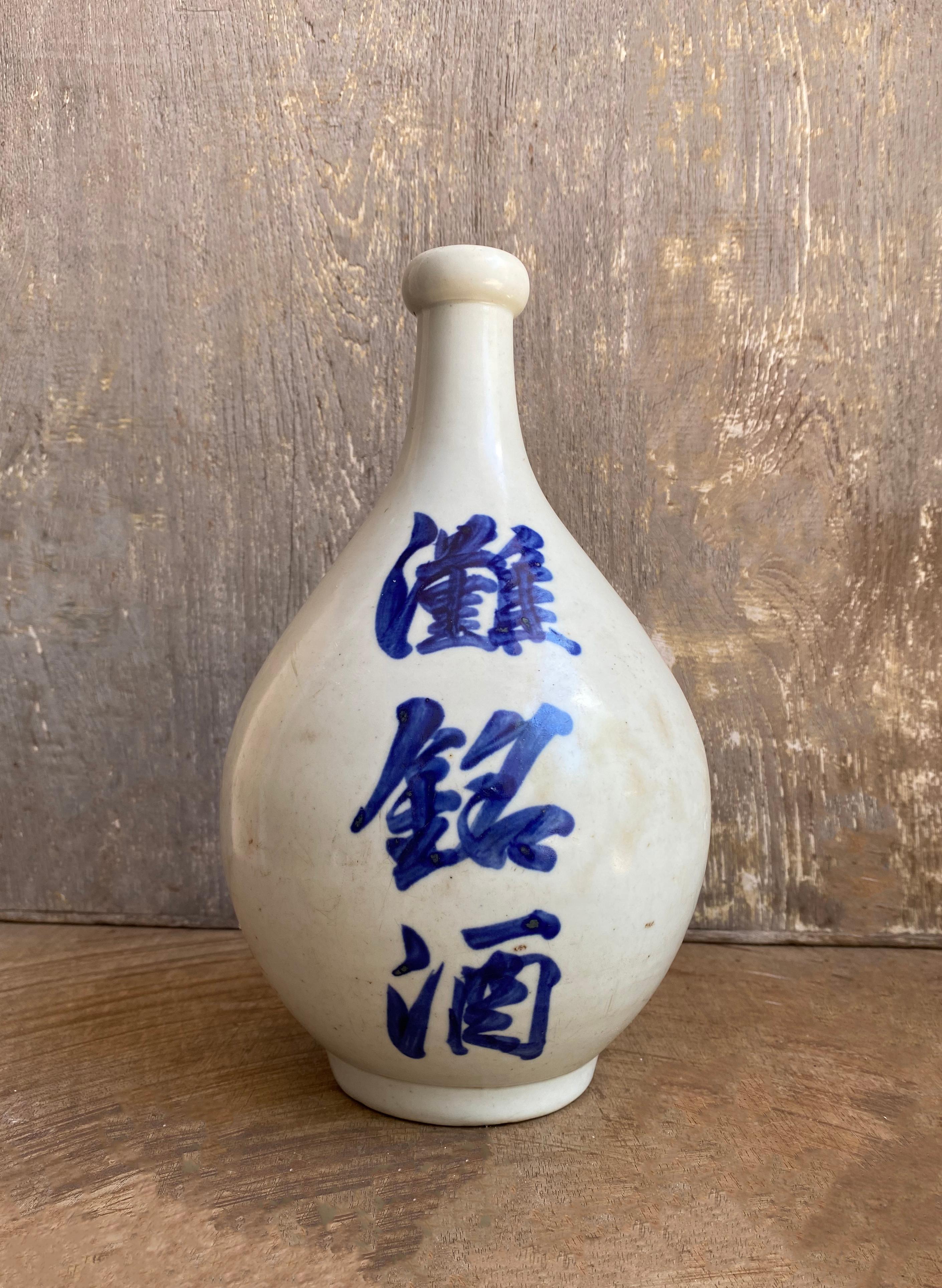 A Japanese ceramic Sake Jar from the early 20th century. The jar features glazed ceramic and hand-painted characters. 

Dimensions: Height 26cm x diameter 14.5cm.

 