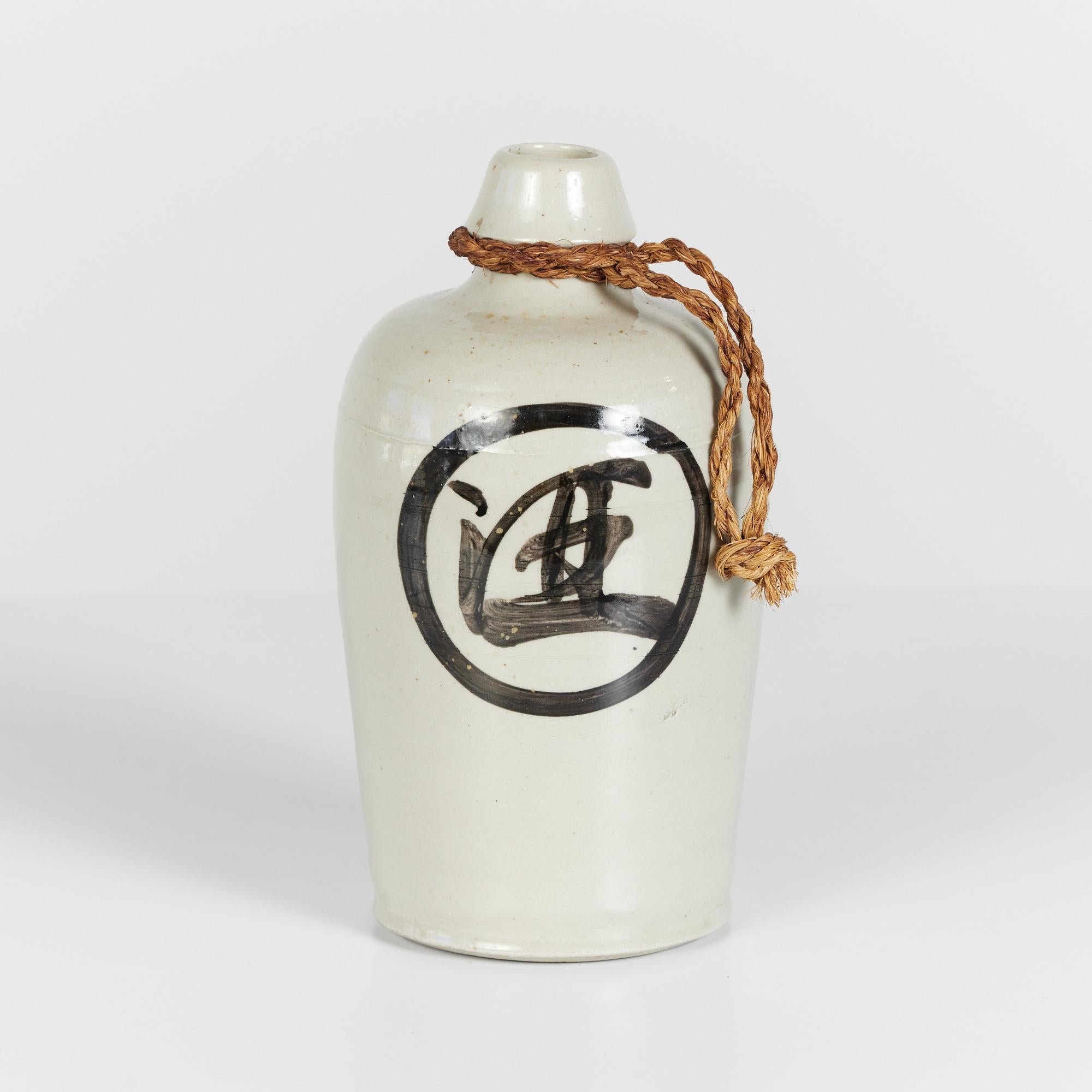 Japanese ceramic vessel traditionally used to serve sake. The jug features a wheel thrown body with a centered spout and rope handle. The piece has an all over cream glaze with hand painted lettering.

Made in Japan.

Dimensions: 5.25” diameter x