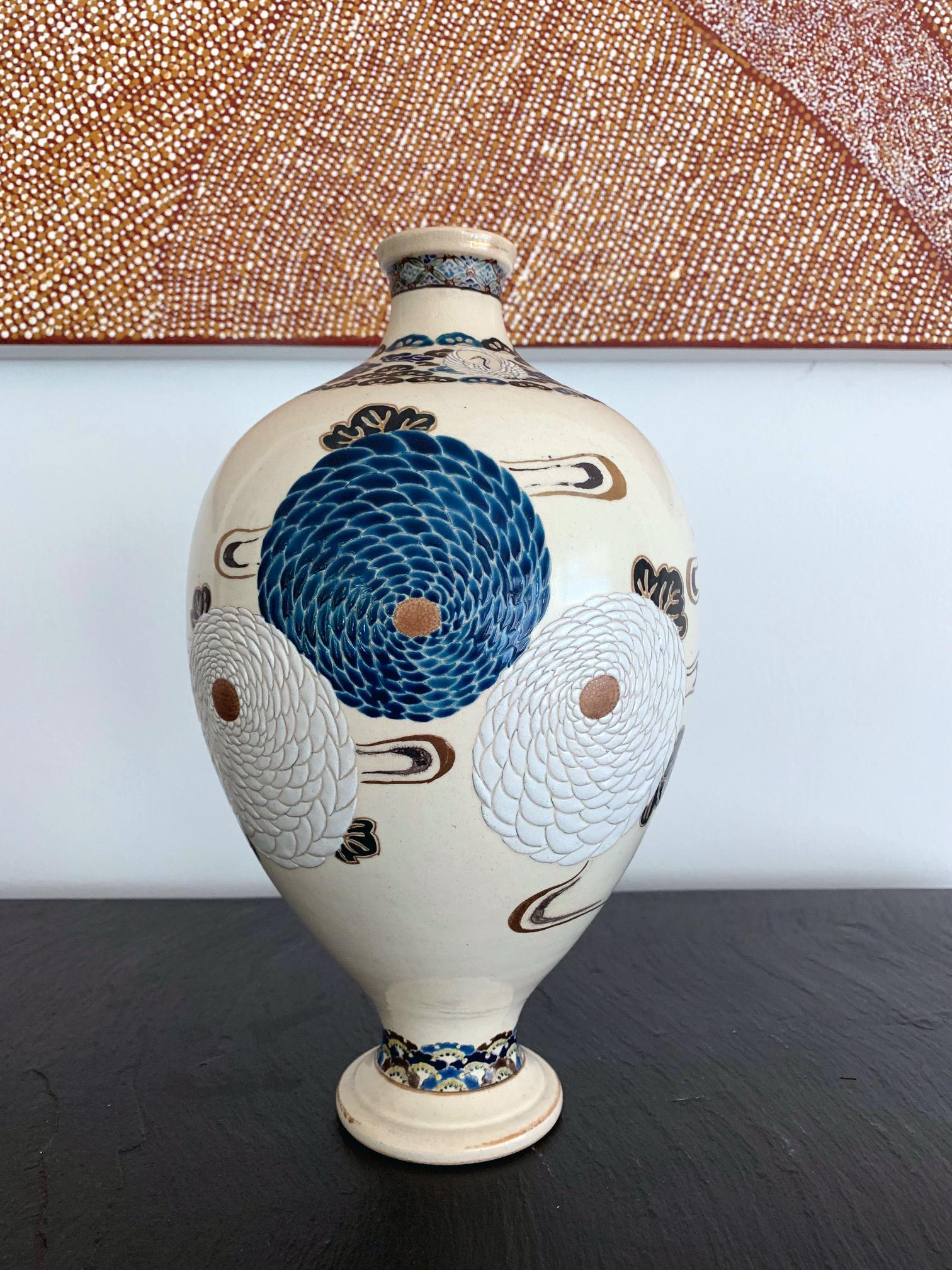 A ceramic vase in an elegant form and fine over glaze decoration. Japanese Satsuma ware that was likely made in Kyoto circa late 19th century. The vase was finely decorated with low relief carving depicting bundles of pompon chrysanthemums in white