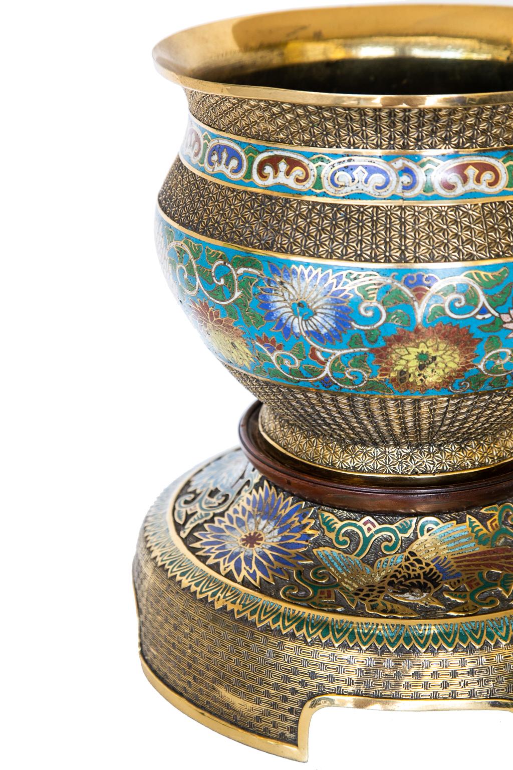 Japanese Champleve’ jardinière on base, with floral motifs in red, white, blue, yellow, and green on this Champleve’ jardiniere. The base has a solid mahogany platform with feet that have arched openings. It is polished and lacquered for easy