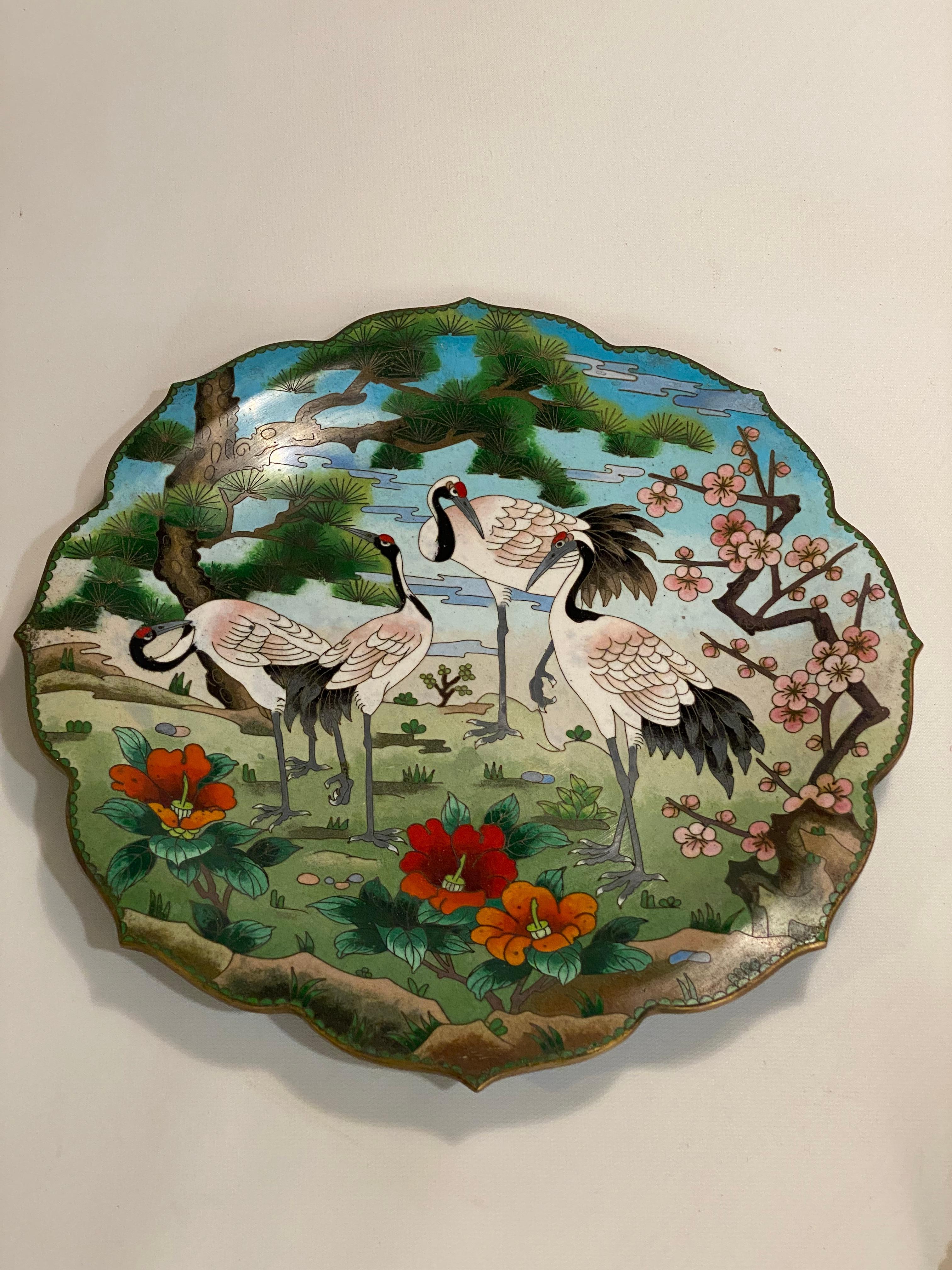 Japanese cloisonne crane decorated plate. Brass and cloisonne. Beautifully and sumptuously decorated in multiple colors with cranes surrounded by flowers and trees. The exterior has a brass floral decoration with a vibrant turquoise enamel. Good