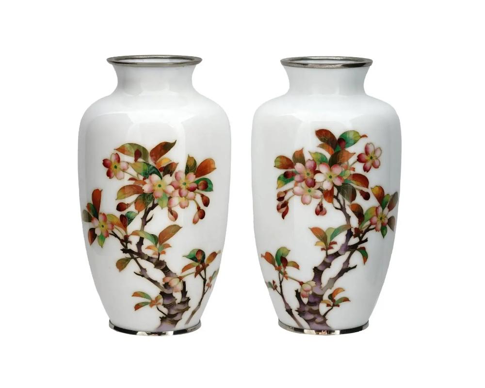 A pair of identical Japanese silver wire and enamel vases, circa: 1940s. The baluster form vases are enameled with polychrome images of blossoming flowers made in the Cloisonne technique on a white ground. Unmarked. Provenance: Mission Gallery. An