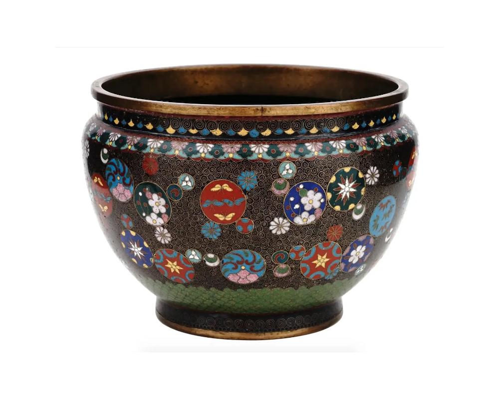 A vintage Japanese enamel over brass cache pot. The ware is enameled with polychrome medallions depicting butterflies, stars, and blossoming flowers, surrounded by floral, swirl and geometrical patterns made in the Cloisonne technique. The neck is