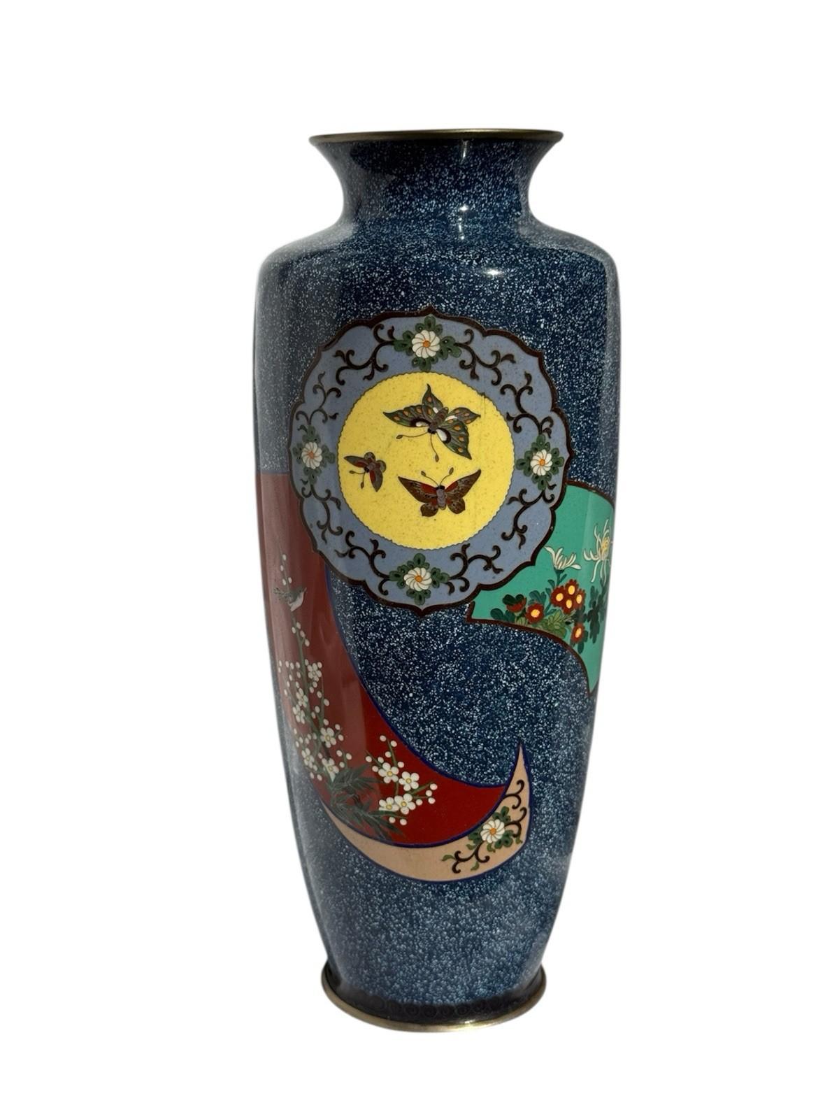 Elegante vaso giapponese in smalto cloisonné alto 9,5 pollici, caratterizzato da un fondo blu intenso con un disegno a nastro fluente in rosso, turchese e crema. Al centro, un medaglione circolare mostra tre farfalle finemente dettagliate su un