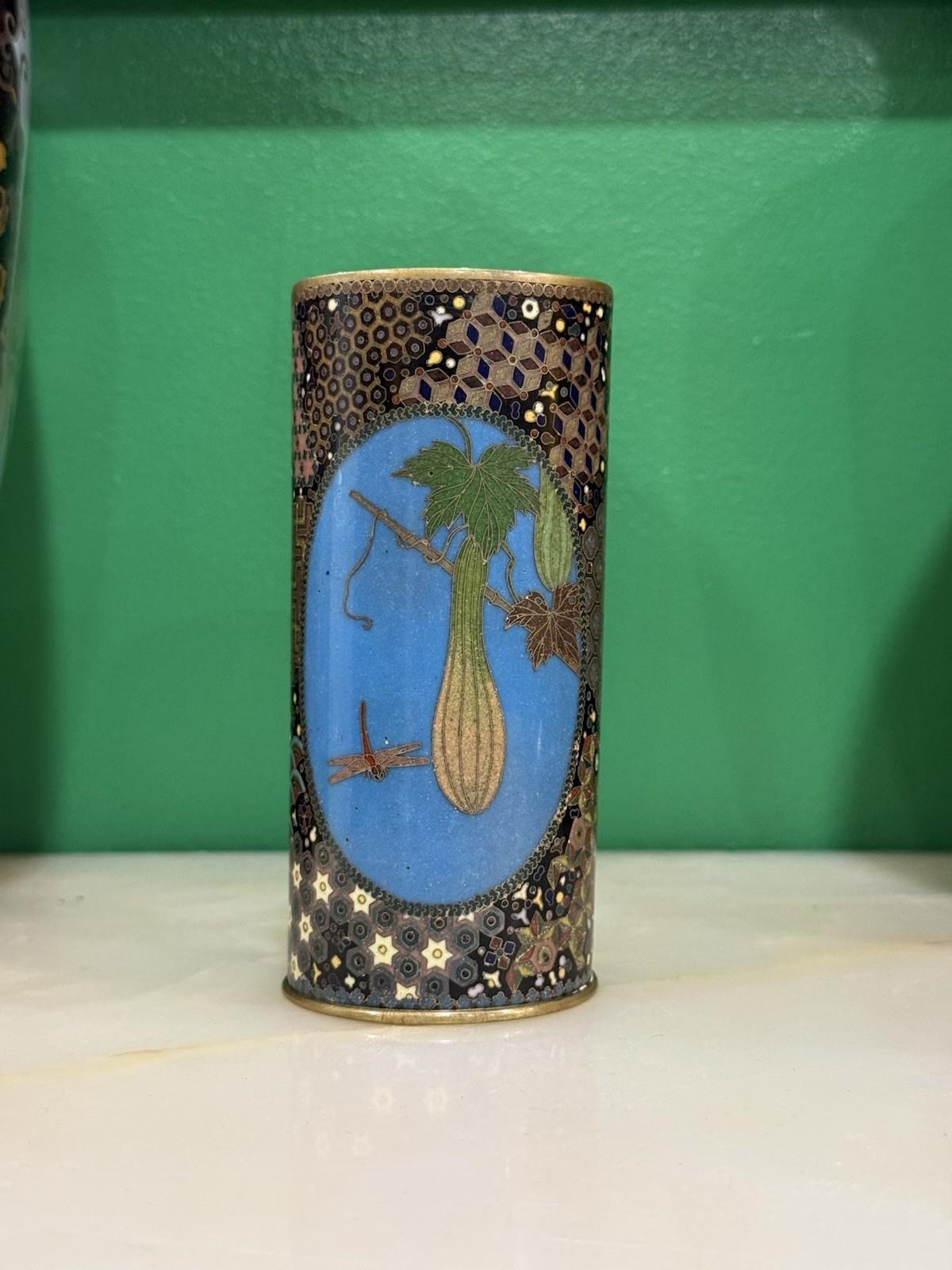 An exquisite Japanese cloisonné enamel vase of cylindrical form, worked in the manner of Gotō Seizaburō, dating to the Meiji period.


One side shows a finely rendered gourd hanging from a vine with a dragonfly hovering nearby, all against a