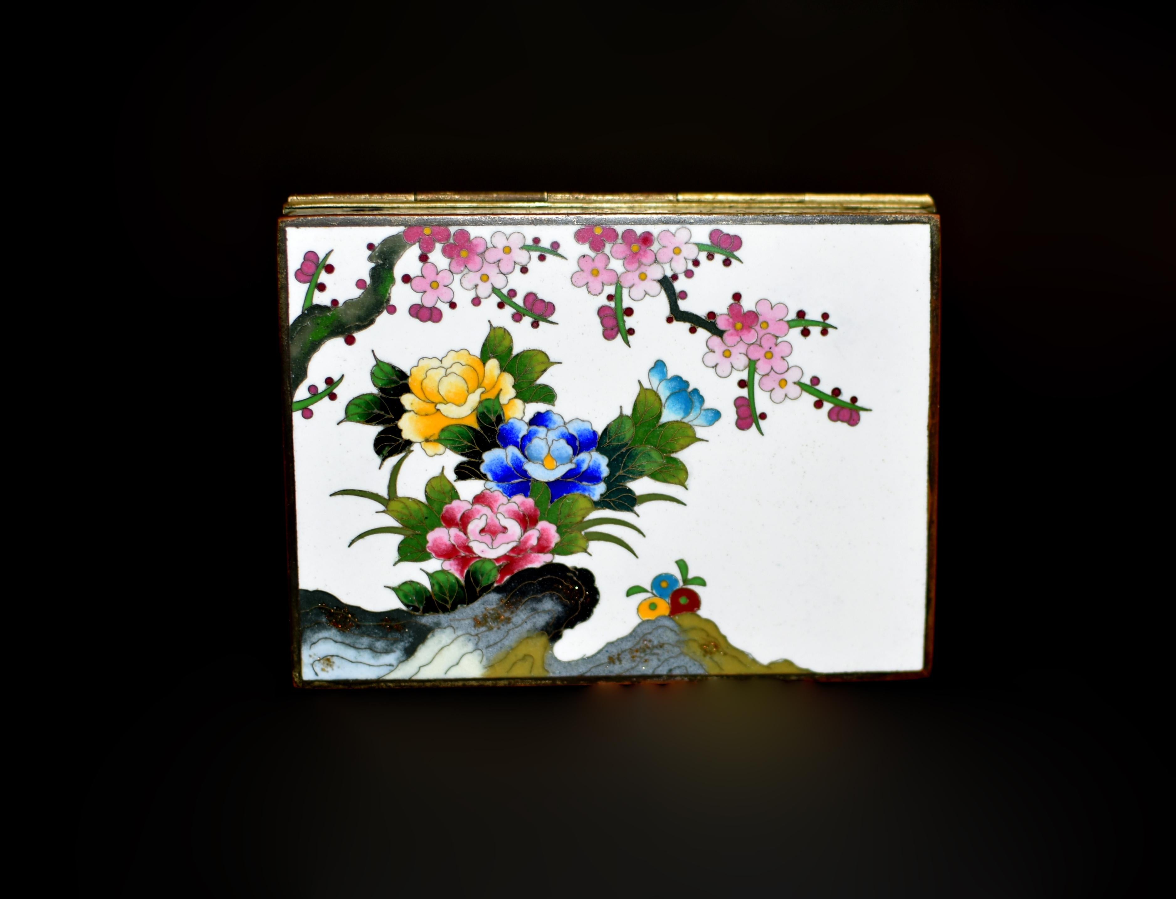 A beautiful Japanese cloisonne box, with mark of Inaba Nanaho, Meiji  period. Worked in various shades of red, blue and yellow enamels depicting three large peonies under a tree of cherry blossom, behind stones adorned with speckles of gold, all on