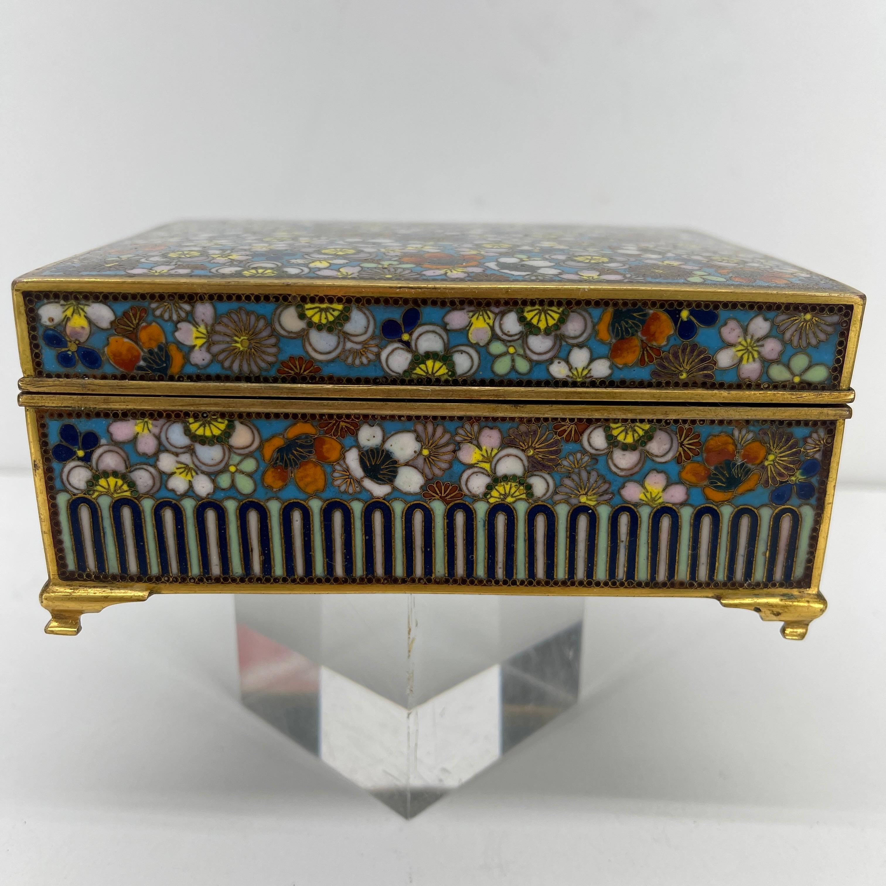 Japanese cloisonné jewelry box, circa 1960s. This beautiful vanity box has gilded delicate legs with petite rounded feet. It's rich floral design top on white enamel background is only enhanced with it's carved interior depicting Mt. Fuji engraved