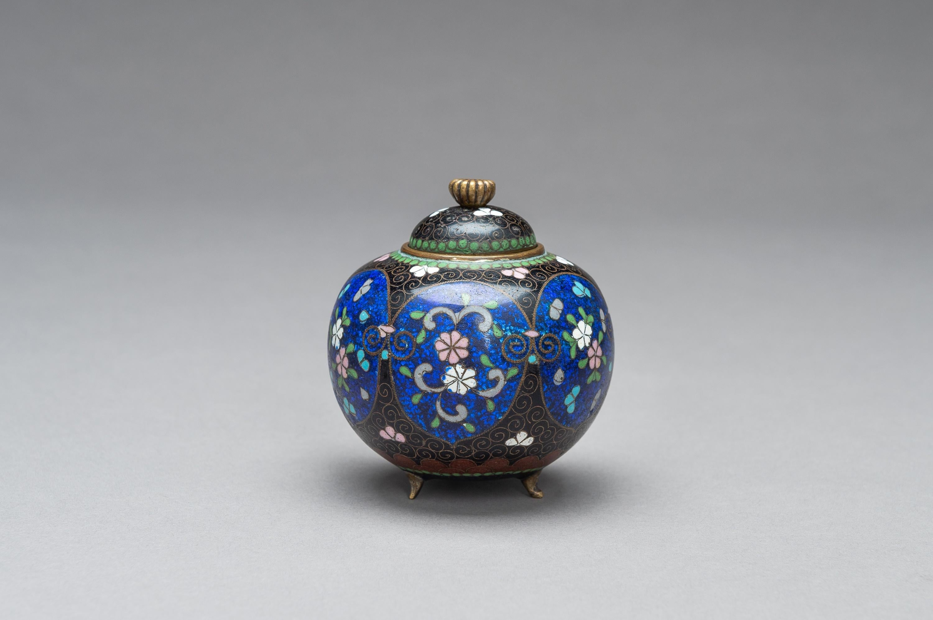 Japanese Cloisonné Koro with cover, Meiji Period (1868-1912)

Of slightly compressed globular form standing on three short curved feet, with domed cover set with a kiku blossom knob, worked in copper wire and colored enamels with floral motifs on