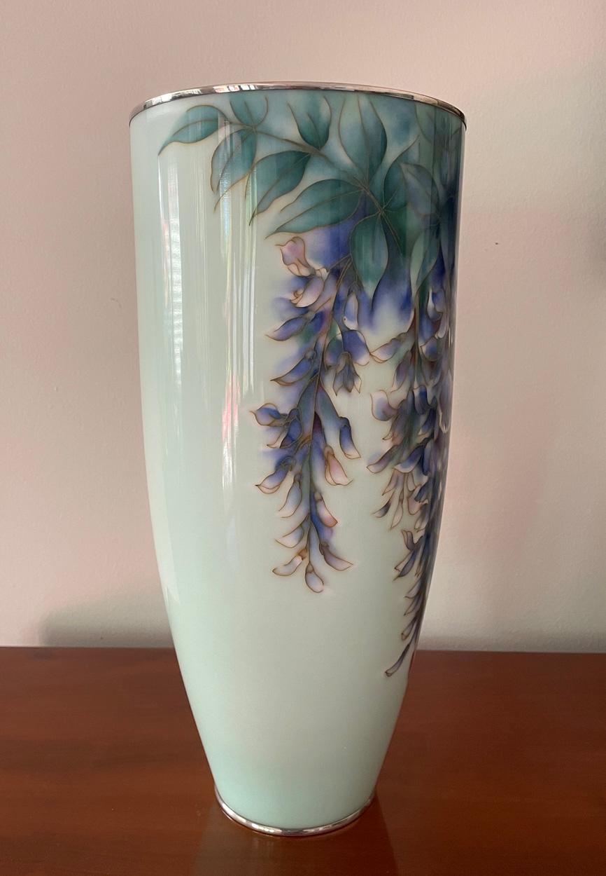 Japanese cloisonne vase, Showa Period (1926 - 1989), the tapering cylindrical body decorated with blue green leaves and drops of elegantly rendered purple, blue and white wisteria on a pale ground, the rims in silver, Ando Studio mark to the base.