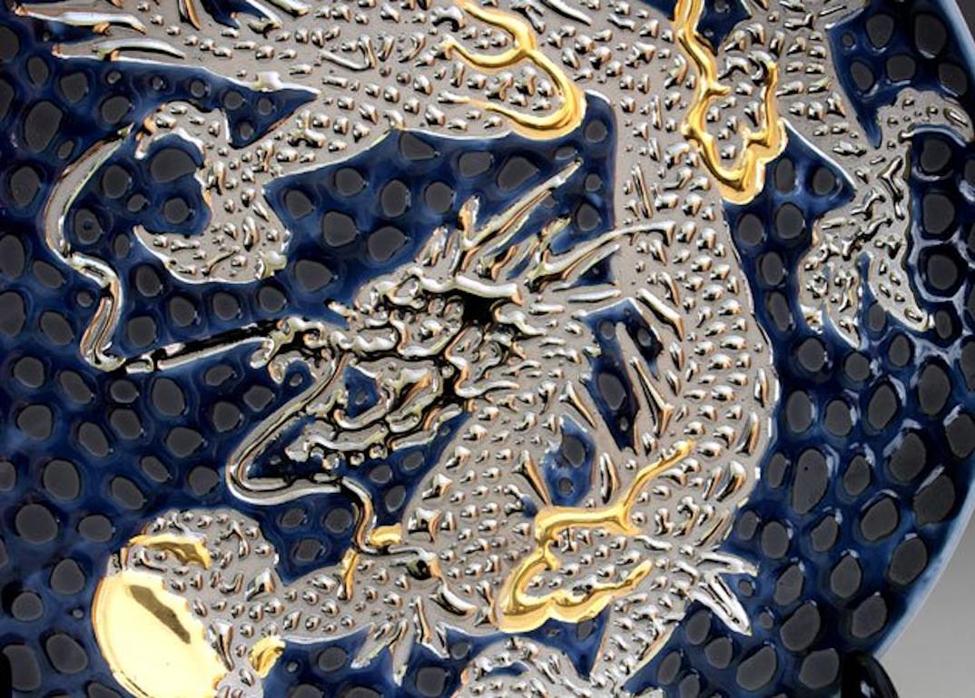 Exquisite contemporary decorative porcelain charger, hand painted showcasing a dramatic scene of a dragon in platinum and gold, set against a dimpled black background, a signed piece from the signature dragon collection by highly acclaimed