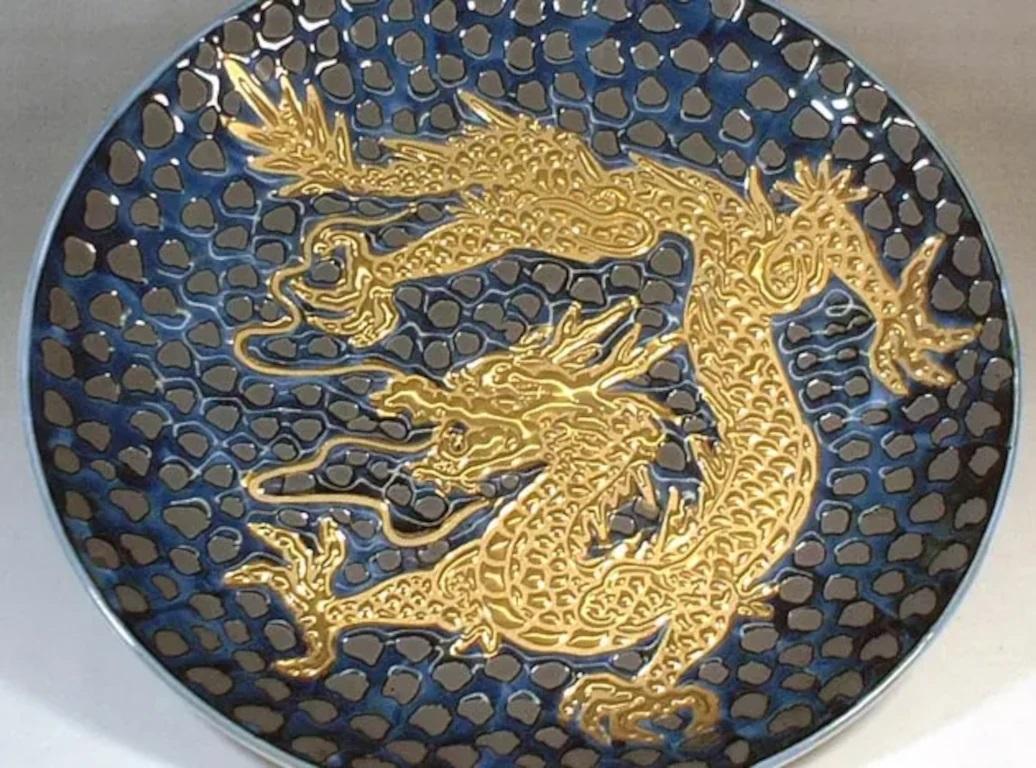Exquisite contemporary decorative porcelain charger, hand painted showcasing a dramatic scene of a dragon in gold, set against a dimpled black background, a signed piece from the signature dragon collection by highly acclaimed award-winning master