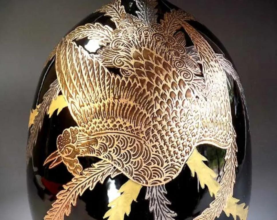 Exceptional Japanese contemporary decorative porcelain vase intricately hand painted, showcasing a dramatic scene of a phoenix in platinum and gold extending its beautiful long wings to cover the entire body of the vase, set against a stunning black