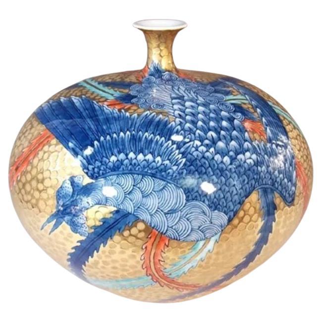 Squisito vaso decorativo giapponese in porcellana a rilievo, intricatamente dipinto a mano in blu sottosmalto, che mostra una scena drammatica di una fenice che estende le sue bellissime ali lunghe, su uno splendido sfondo dorato a rilievo. Si