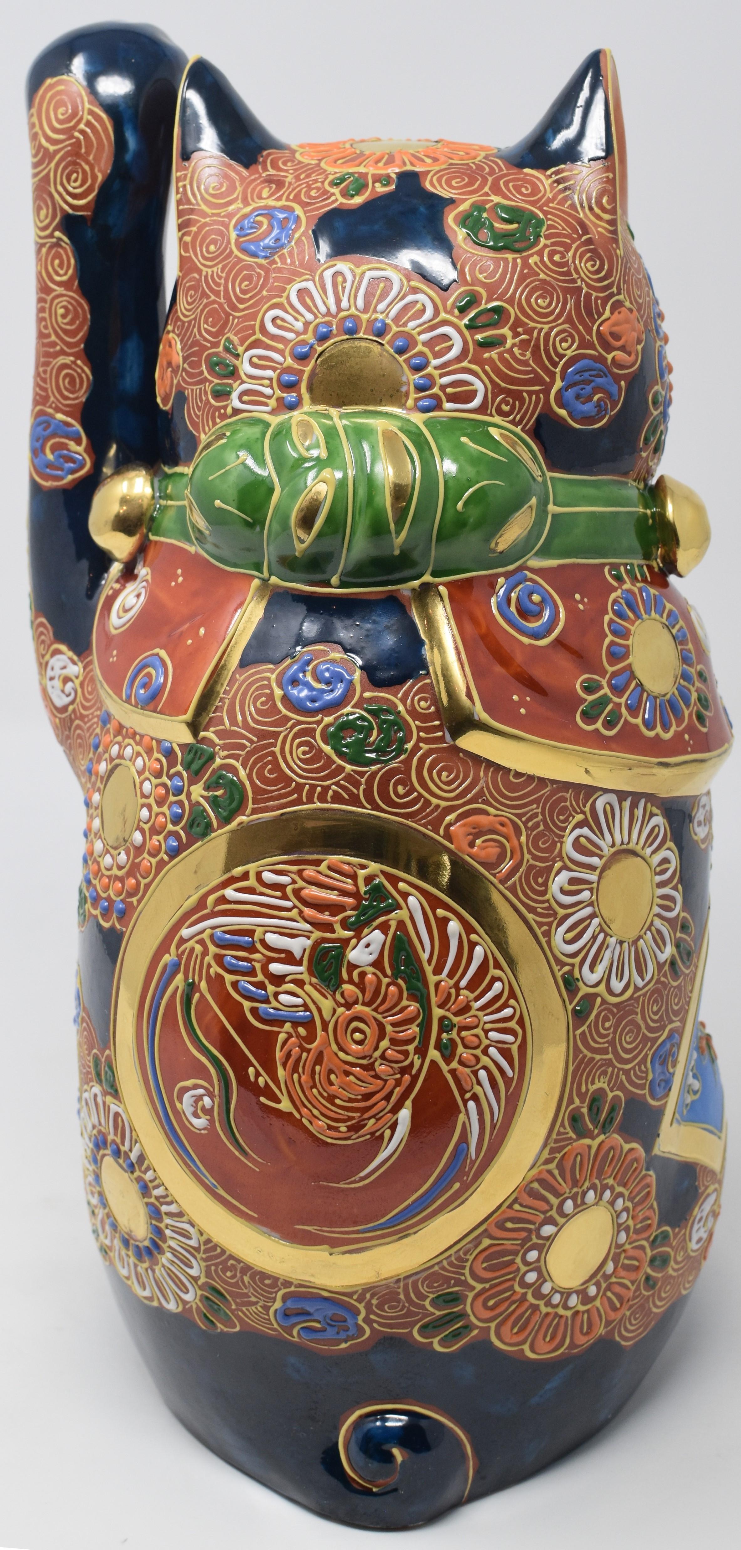 Japanese Contemporary beckoning cat, a uniquely gilded and hand painted porcelain piece from the Kutani region of Japan. The cat raising his left paw is adorned with multiple golden medallions and is covered with raised loops characteristic of the