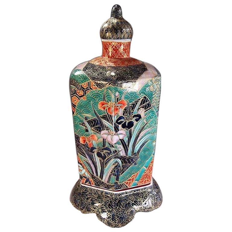 Exquisite contemporary Japanese decorative porcelain lidded jar, intricately hand painted in black, green and red with generous gold details, showcasing patchwork of overlapping floral and geometric panels on a stunning black background with gold