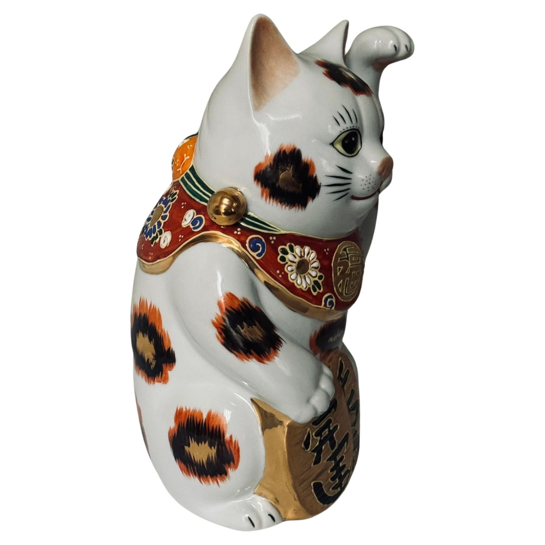 Charming beckoning cat with left paw raised is a gilded and hand painted porcelain piece from the Kutani region of Japan.
The beckoning cat comes in two varieties. The more common right-handed beckoning cat (with right paw raised) is said to bring