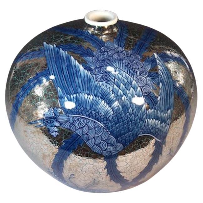 Exceptional Japanese contemporary decorative porcelain vase, intricately gilded in platinum and hand painted, boasting a dramatic phoenix in deep blue underglaze, extending its beautiful long wings to decorate the surface of the vase, set against a