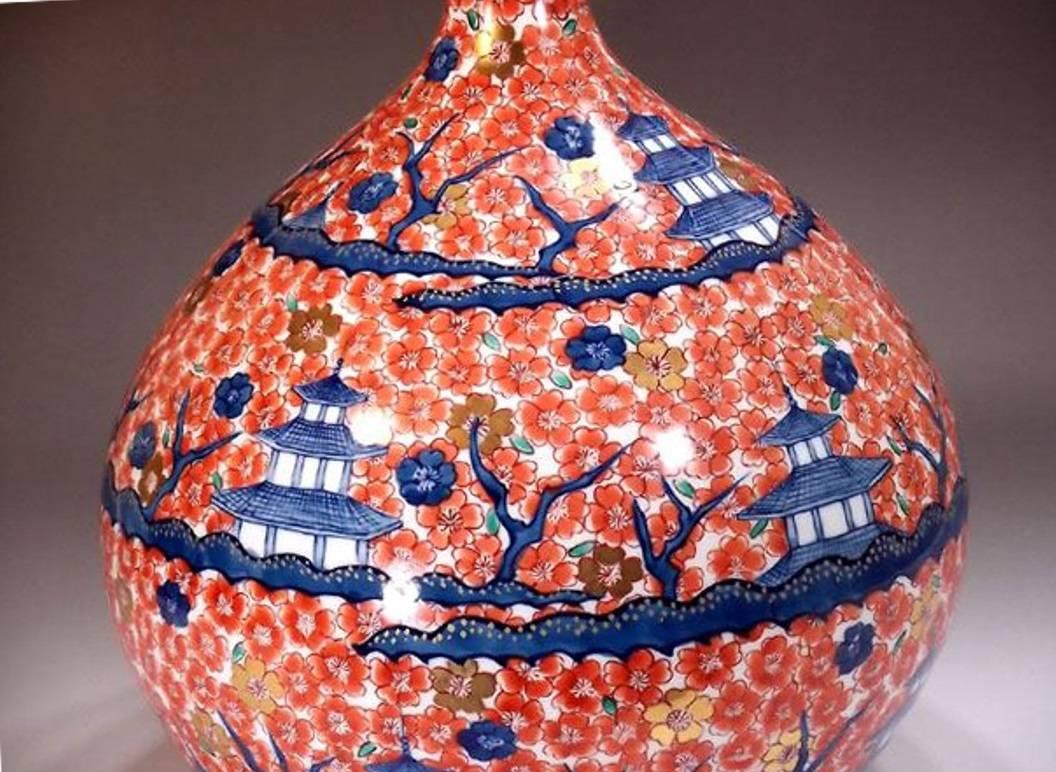 Mesmerizing Japanese contemporary large porcelain decorative vase hand-painted on an elegant bottle shape body, depicting plum blossom in red and medieval palaces in shades of blue and details in gold, a signed masterpiece by highly acclaimed