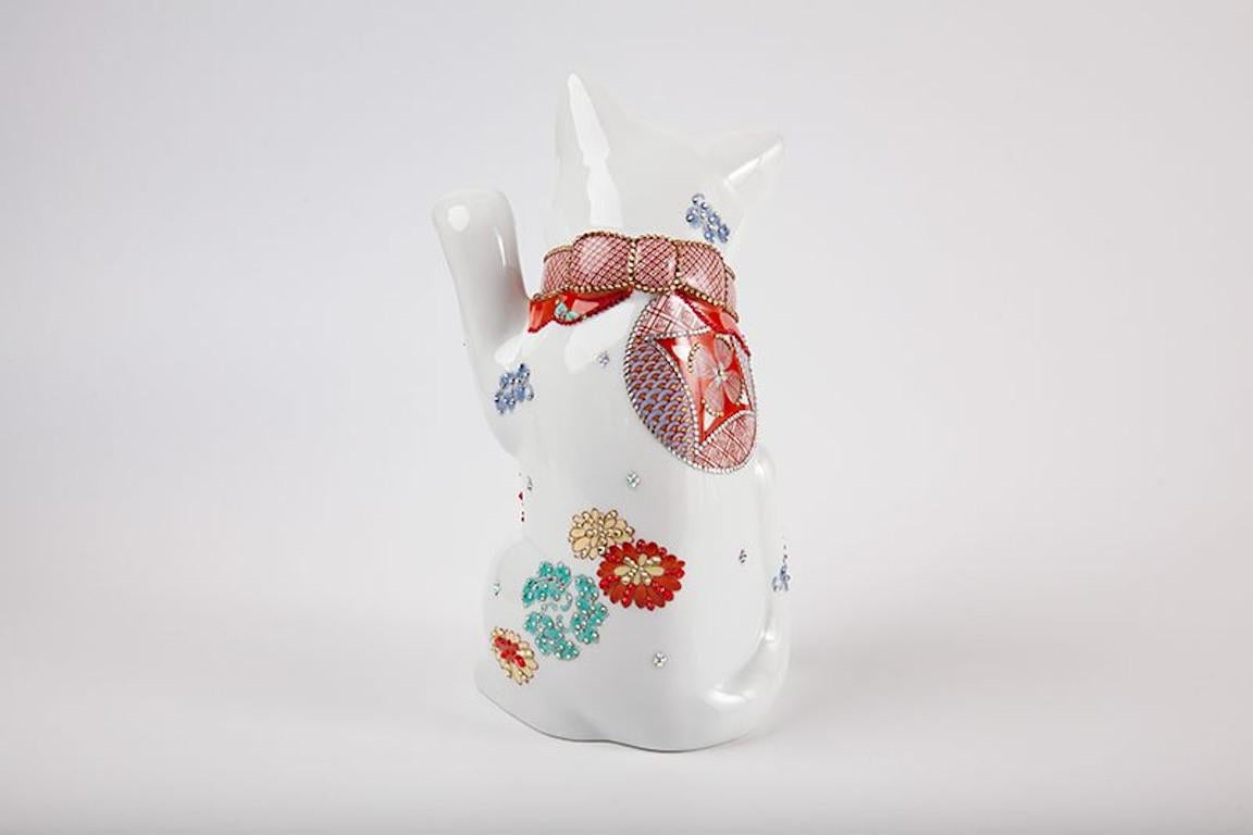 Contemporary Japanese lucky cat (maneki neko,) raising his right paw. Swarovsky crystals generously adorn this stunning lucky cat with intricate pattens in red, white, blue and gold. The red kerchief has a knotted amulet in the back. While the
