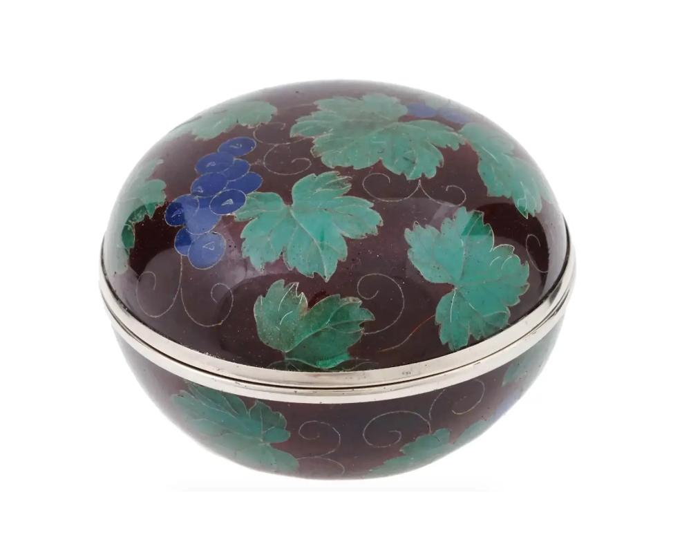 A Japanese covered silvered and enamel kogo or box for incense. The box is enameled with polychrome images of grape vines with berries made in the Plique a Jour technique on burgundy ground. Marked or probably numbered, on the bottom. Circa: the