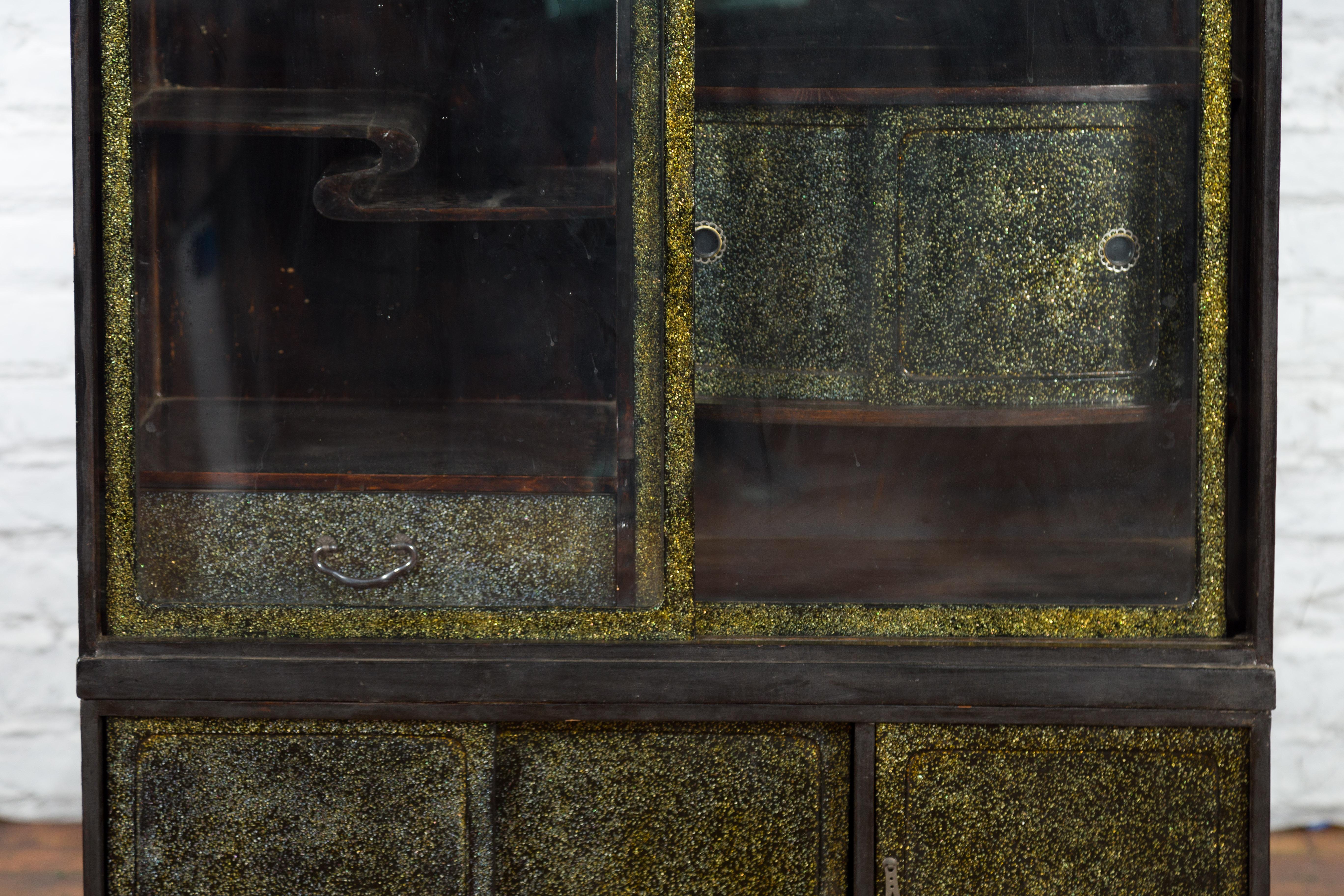 A Japanese compound cabinet from the early 20th century with black and gold speckled finish and glass sliding doors. Created in Japan during the early years of the 20th century, this compound cabinet features a linear silhouette perfectly