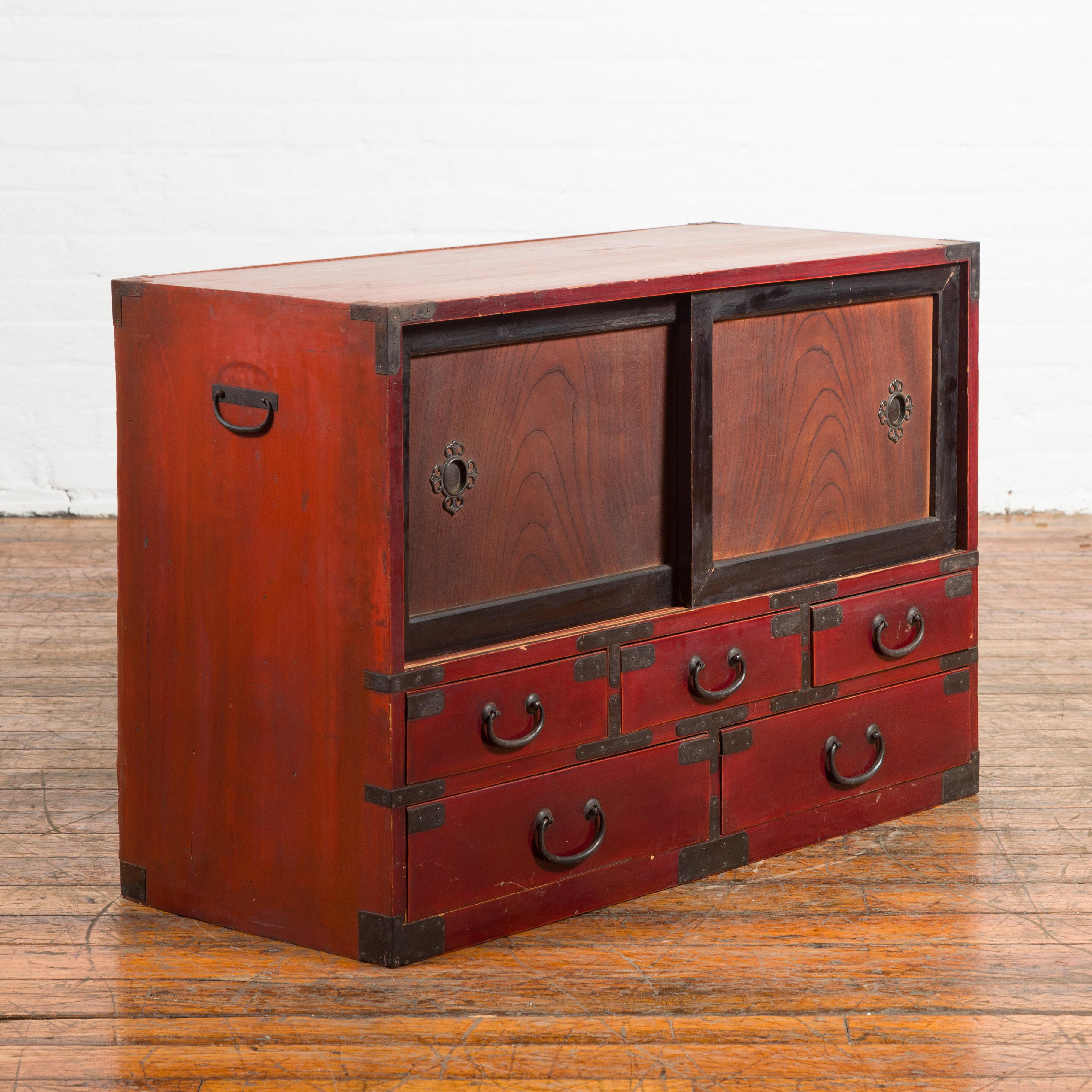 A Japanese dark red and black lacquered tansu cabinet from the early 20th century, with five drawers and two sliding doors. Created in Japan during the early years of the 20th century, this low cabinet features a dark red lacquered body highlighted