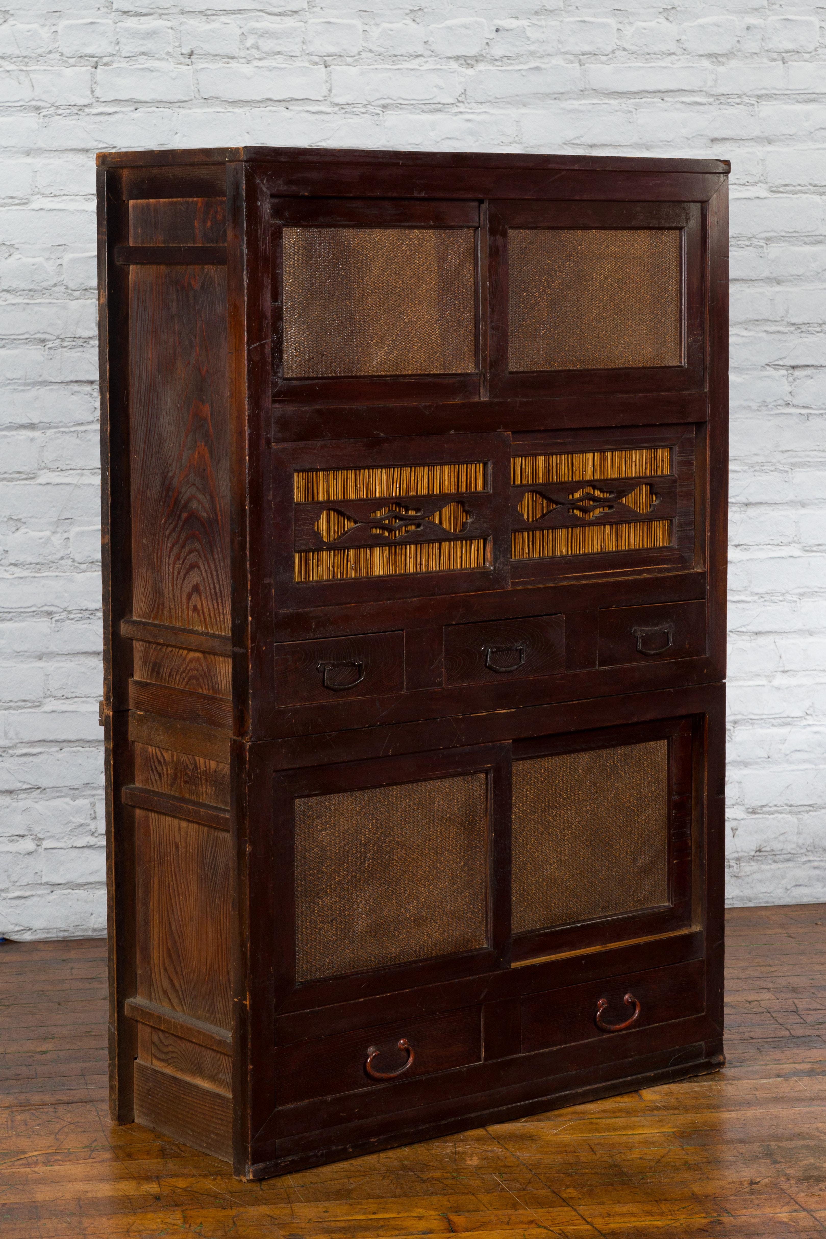 An antique Japanese tansu cabinet from the early 20th century, with sliding doors, drawers, reed and rattan design. Created in Japan during the early years of the 20th century, this tansu cabinet features a dark lacquer perfectly contrasted by