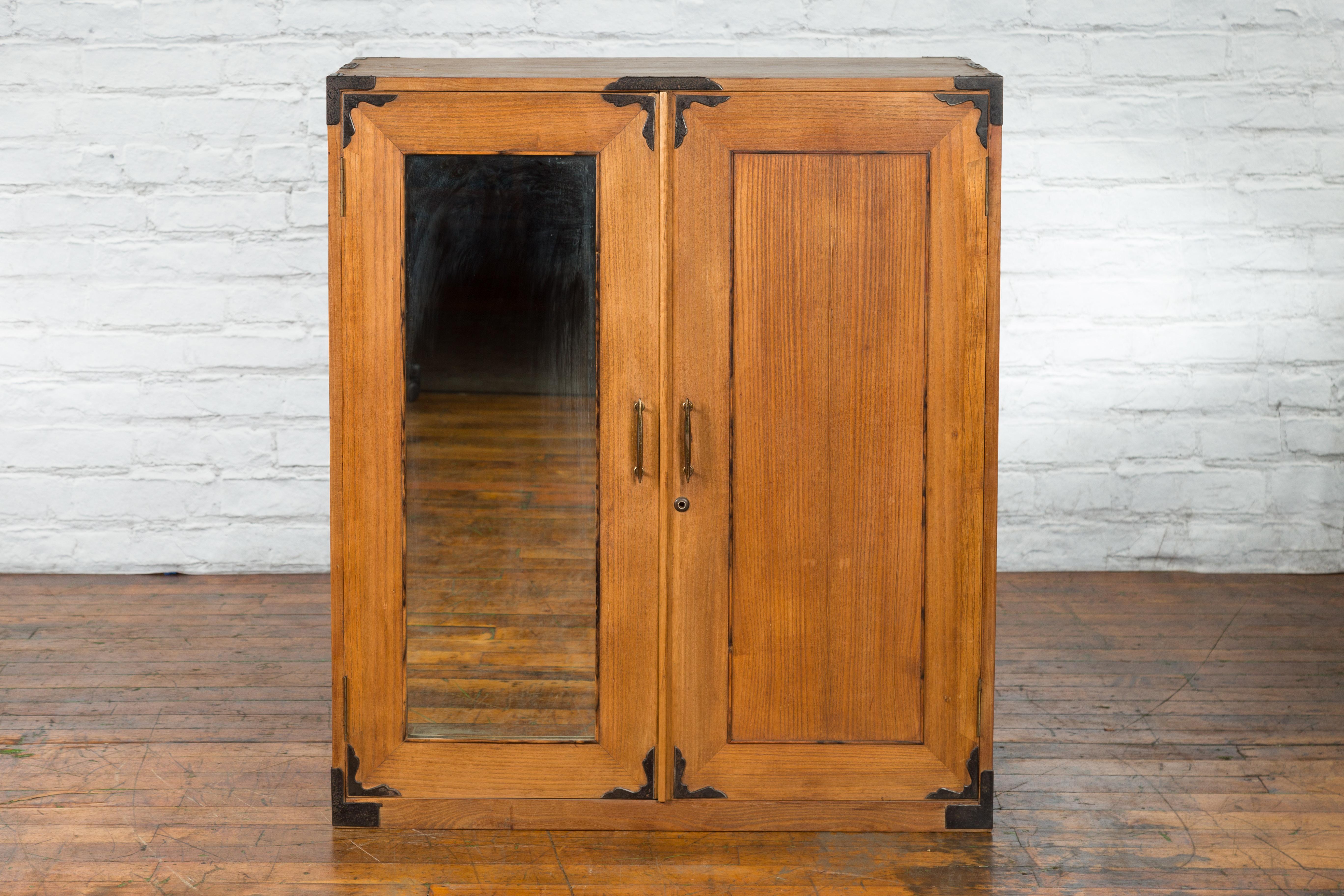 An antique Japanese Tansu clothing cabinet from the early 20th century, with mirrored door and iron hardware. Created in Japan during the early years of the 20th century, this tansu cabinet features a rectangular top with iron braces, sitting above
