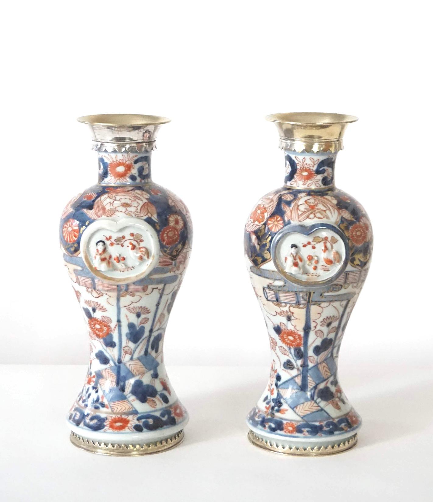 A wonderful and rare near pair of first quarter 18th century Japanese Edo Imari garniture vases of baluster form having silver-gilt paktong neck and foot mounts in traditional imari color palette of underglaze blue and overglaze iron red and gold