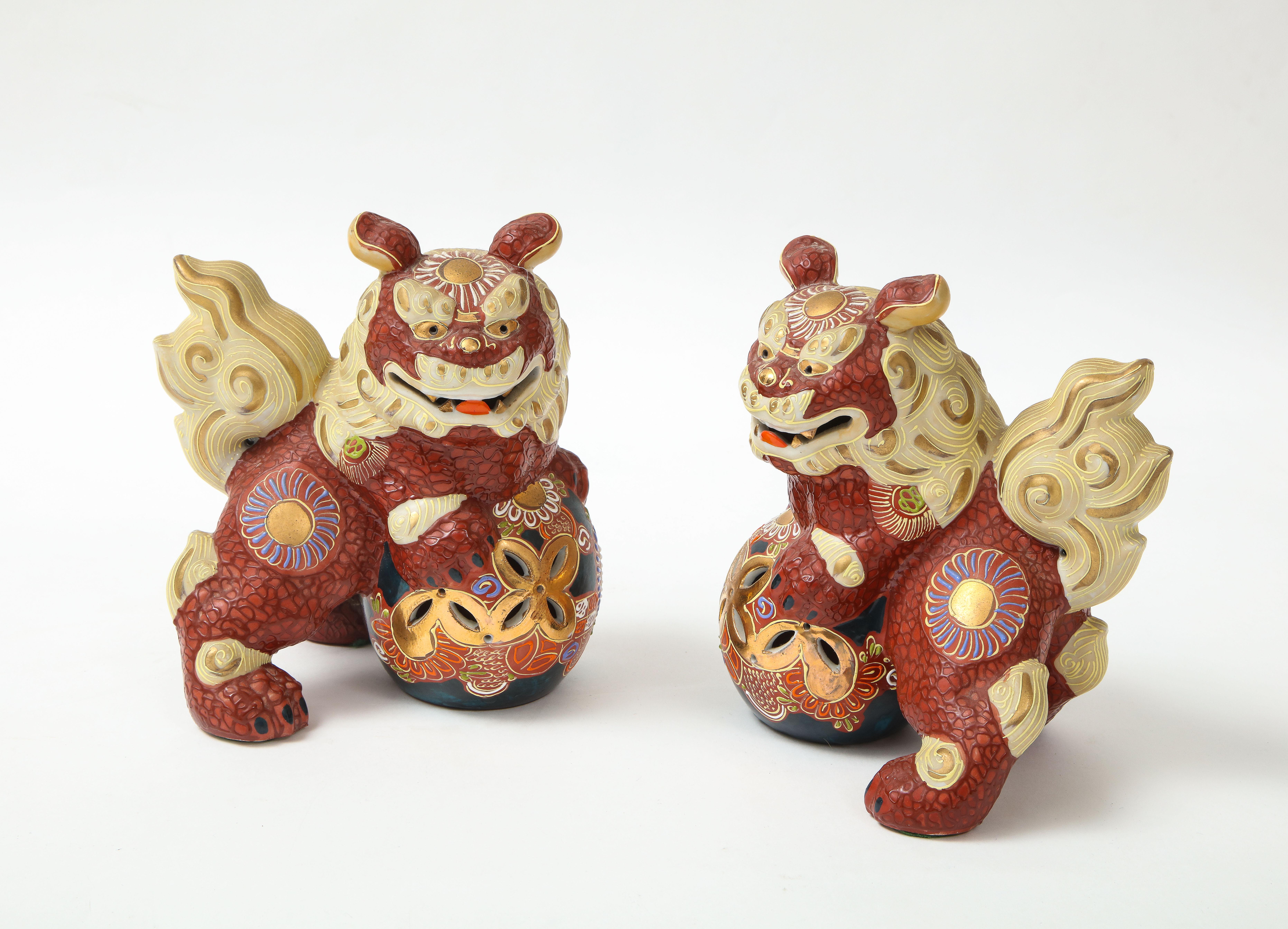 Pair of mid century hand decorated porcelain foo dogs featuring a cinnabar ground accented with colorful glaze polychrome and gold accents.