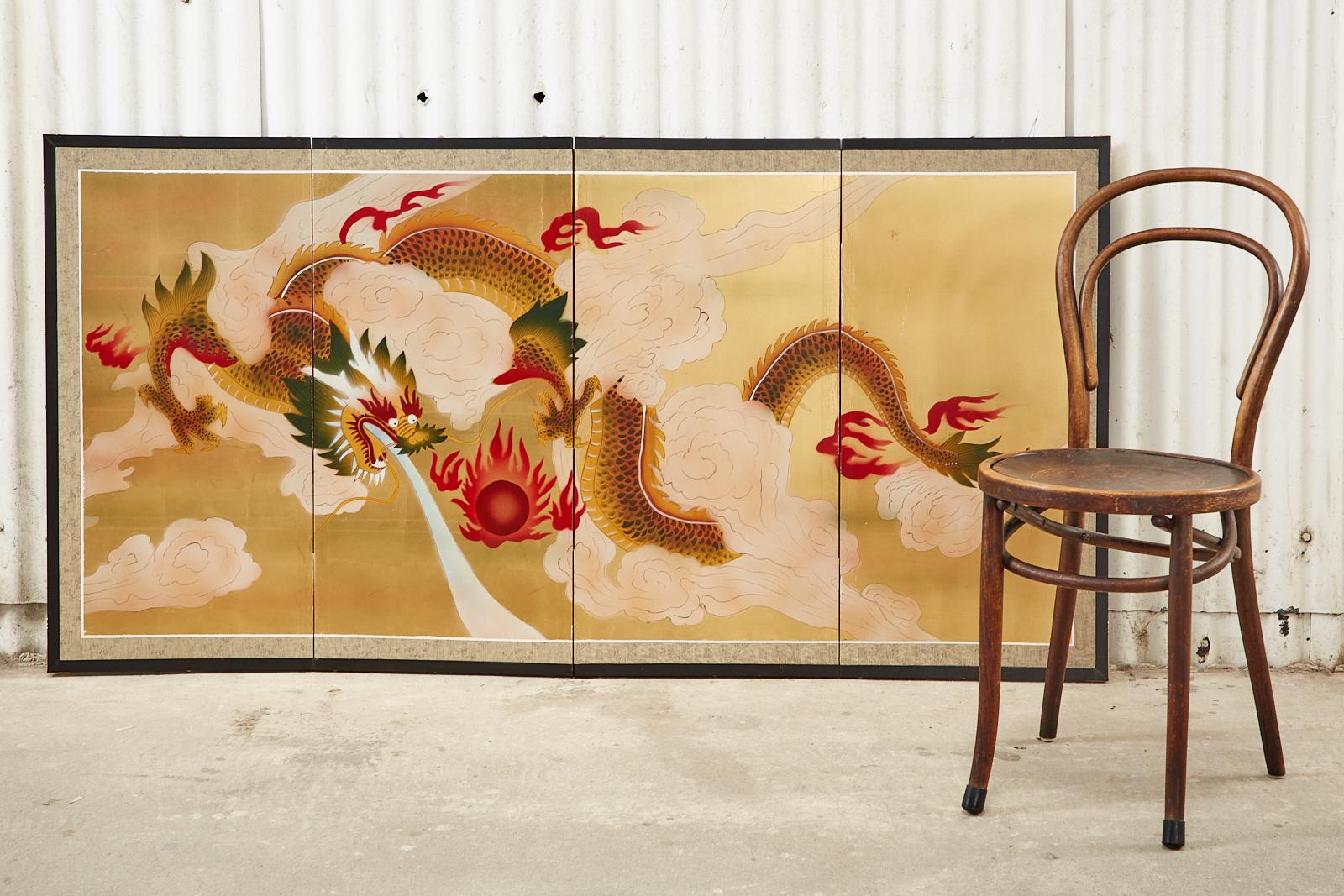 Dramatic Japanese four-panel byobu screen depicting a dragon in the clouds against a gold leaf square background. Chasing a flaming red jewel or sun amid large white clouds. Ink and color pigments on a gold leaf ground set in a black lacquered frame