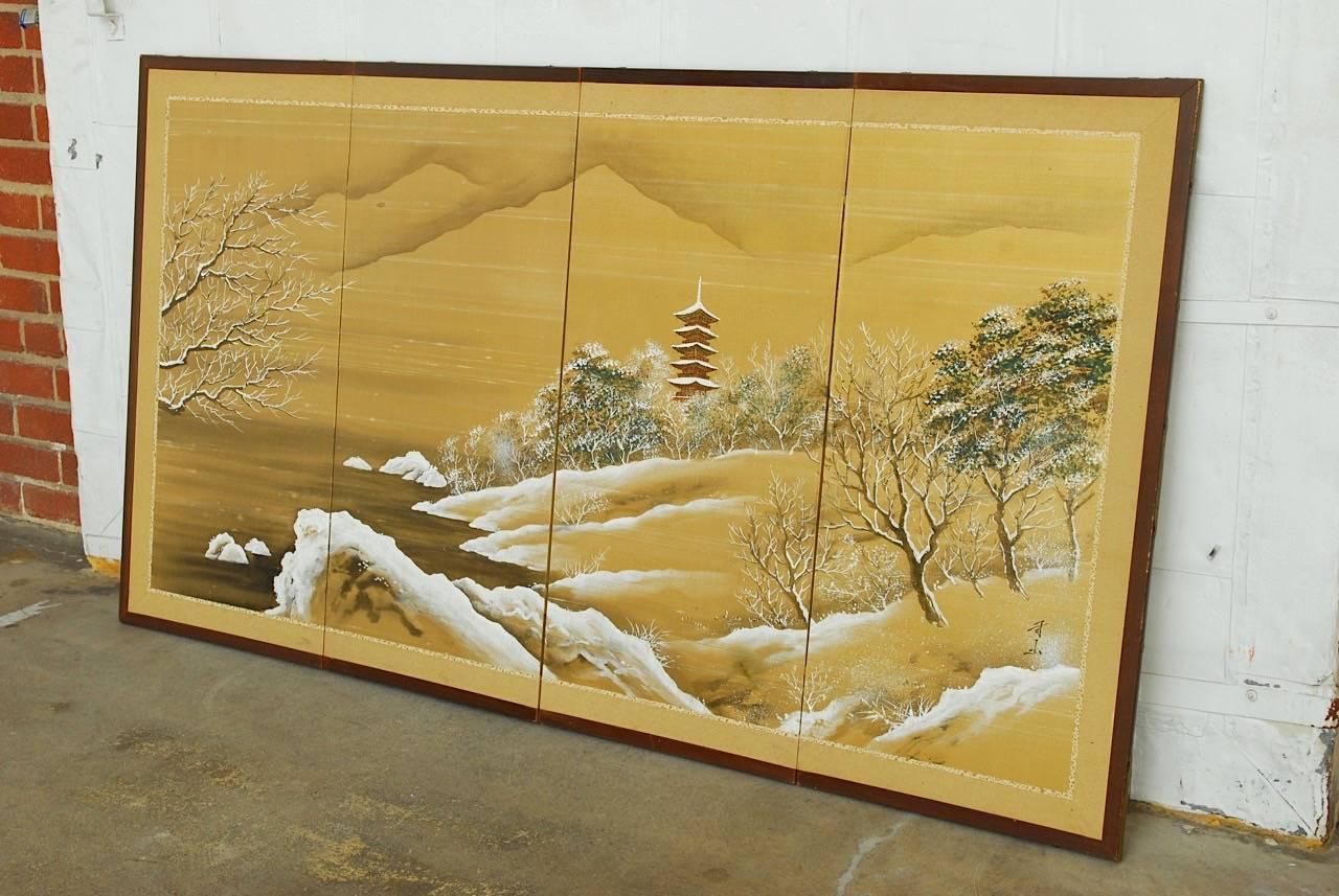 Idyllic Japanese four panel painted silk Byobu screen depicting a snow covered landscape with a pagoda. Intricate trees and foliage delicately covered with snow under a cloudy sky set in a wooden frame with two brocade border accents. The corners