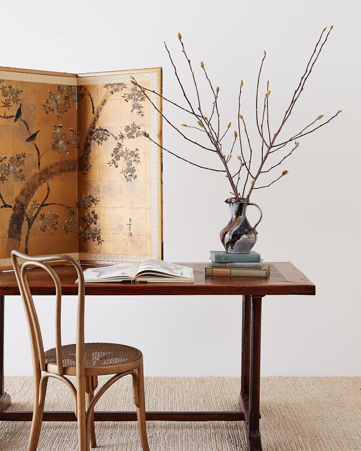 Midcentury Japanese four panel byobu screen depicting blue birds in a blossoming cherry or prunus tree. Painted on squares of gold leaf and set in a wooden gilt frame with patinated brass accents. Bordered with a brocade silk in a light rose gold