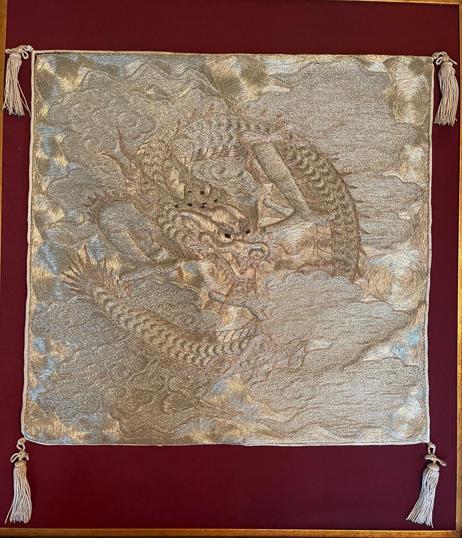 A visually stunning Japanese fukusa panel with an embroidered dragon on a swirling cloud background, nicely displayed on a scarlet felt matt in a carved black wood frame with an antique-finish rose gold trim. This piece of textile art is likely