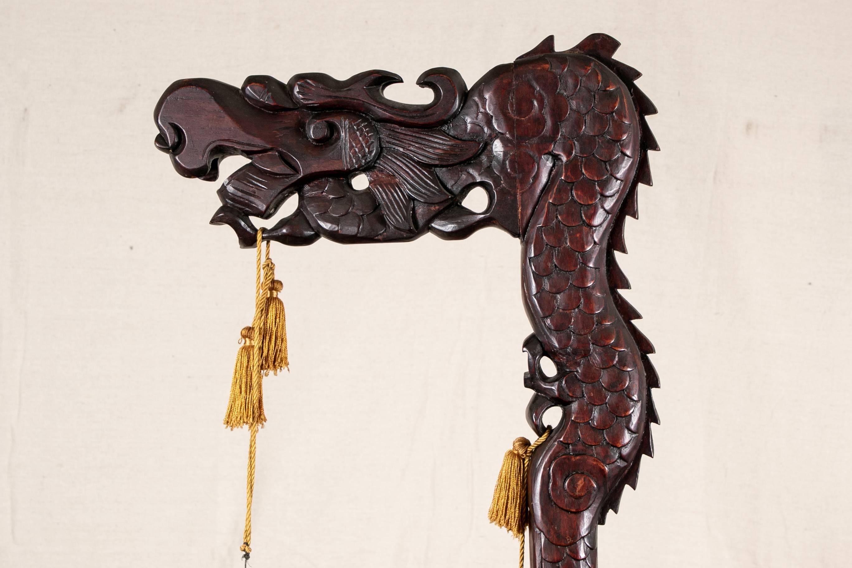 Asian bells on a carved rosewood dragon stand, three tiers of black metal bells with brown enamel decoration of leaves and geometric bands. Suspended on a tall carved rosewood dragon form stand with scales and a scrolled head. Silk cords and