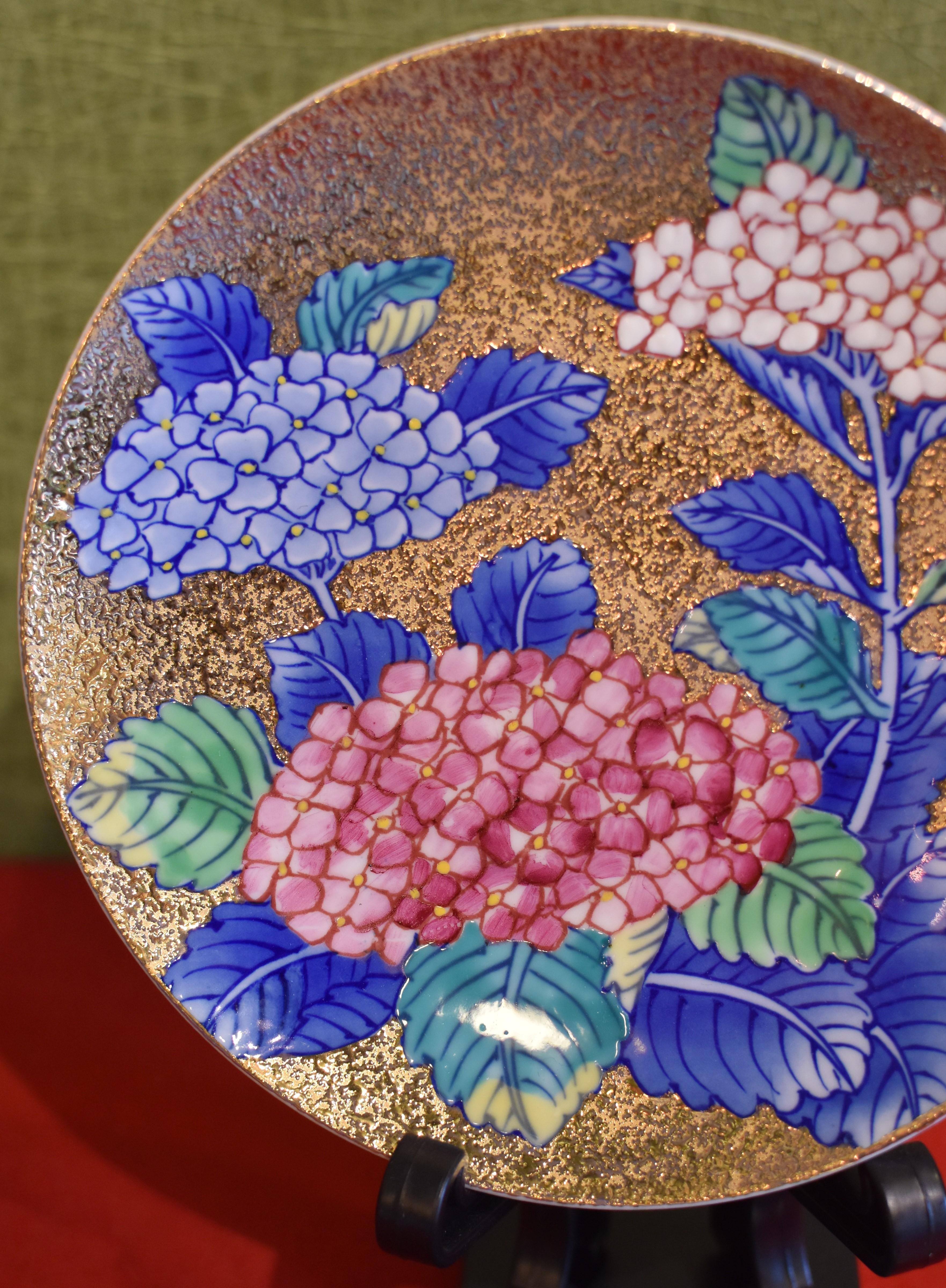 Exquisite zeitgenössische Tasse und Untertasse aus vergoldetem japanischem Porzellan, aufwändig handbemalt in lebhaftem Blau, Rot und Weiß auf einem attraktiven vergoldeten Korpus, mit herrlichen Hortensien in voller Blüte. Diese Tasse mit