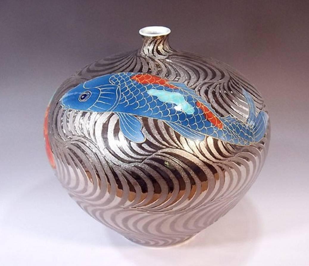 Elegant contemporary Japanese hand painted decorative porcelain vase in a beautiful ovoid shape featuring two koi carp rendered in iron-red and blue swimming through platinum-gilded wave patterns, combined with a generous use of gold outlining is a