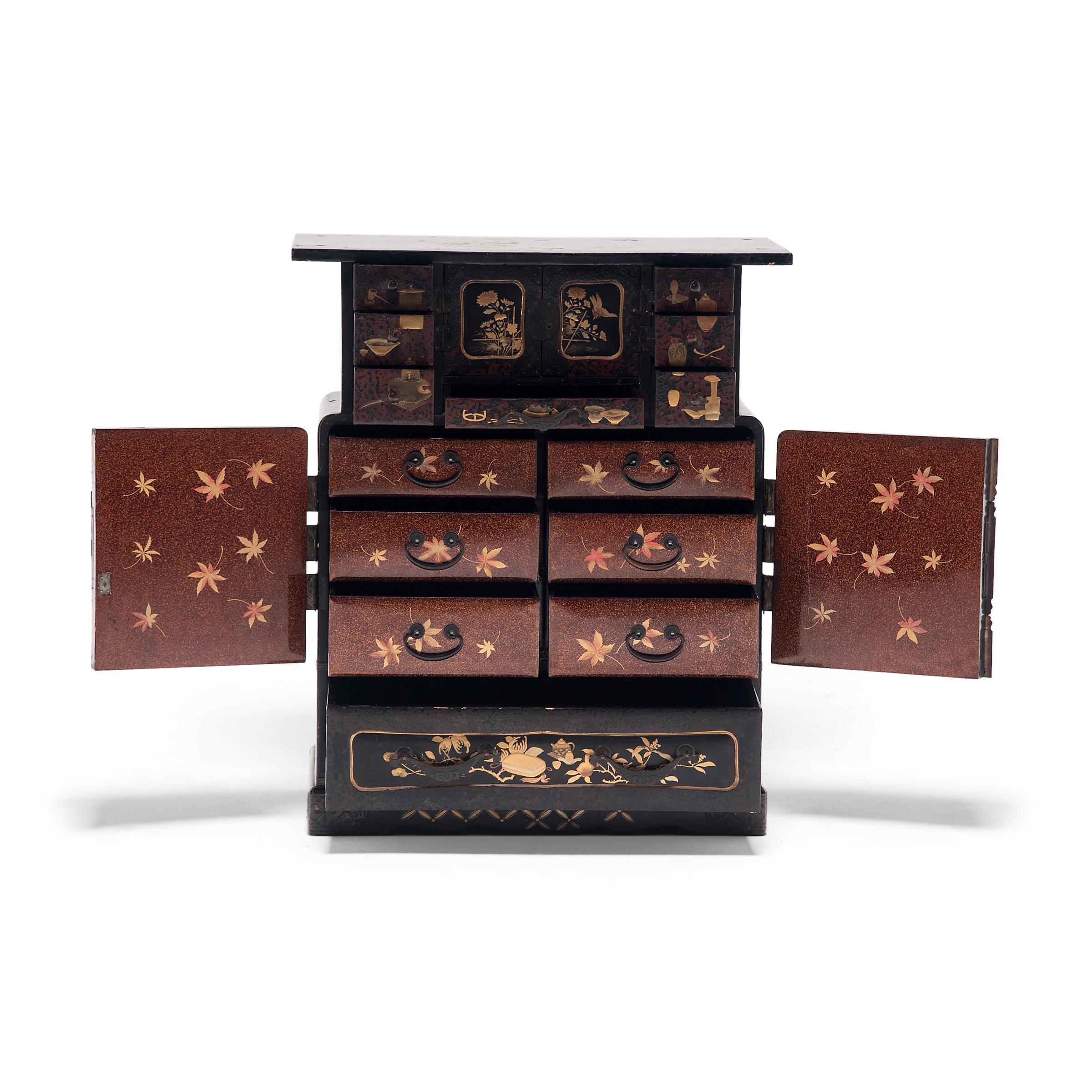 With intricate construction and exquisite decoration, this fine tabletop tea chest is a true masterpiece of Japanese cabinetry and lacquerware. Decorated in gilt with cartouches enclosing birds and maple branches, the mid-section doors enclose