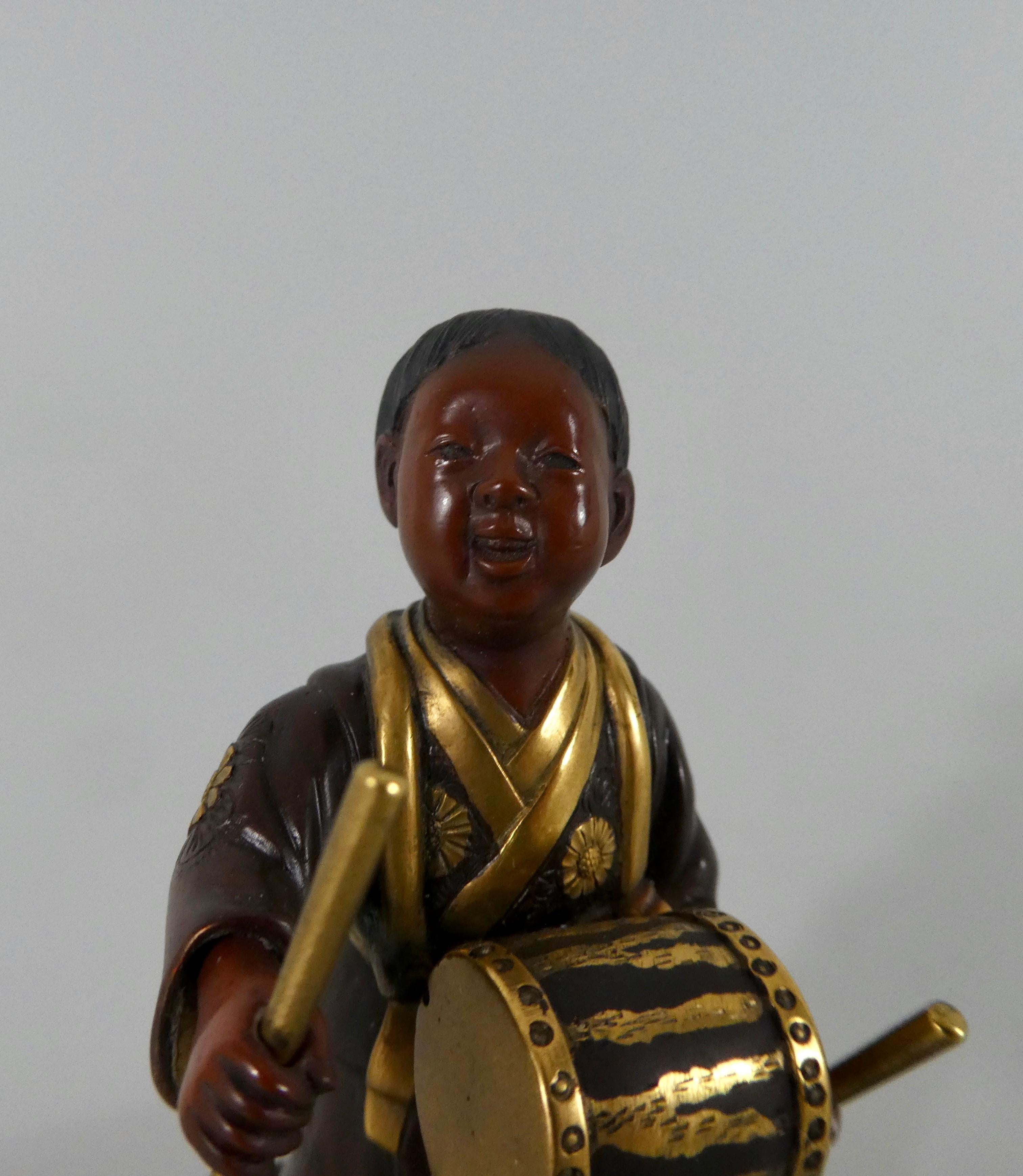 Japanese gilt bronze okimono in Miyao style, Meiji Period (1868-1912). Well modelled as a young smiling boy beating a drum, hung around his neck. His kimono engraved with flowers, and tied with at his back, with a large bow. The details finely