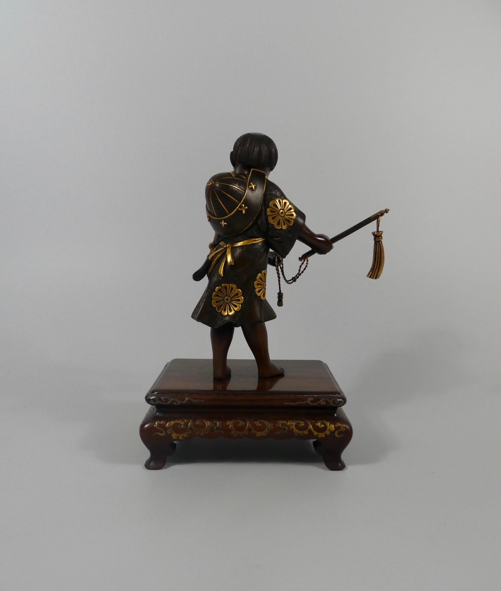 A fine Japanese bronze okimono, by Miyao Eisuke, Meiji Period (1868-1912). Charmingly modelled as a young, smiling boy, dressed as a Samurai. He stands, wearing a knee length tunic, cast and engraved with stylised floral motif, the flower heads