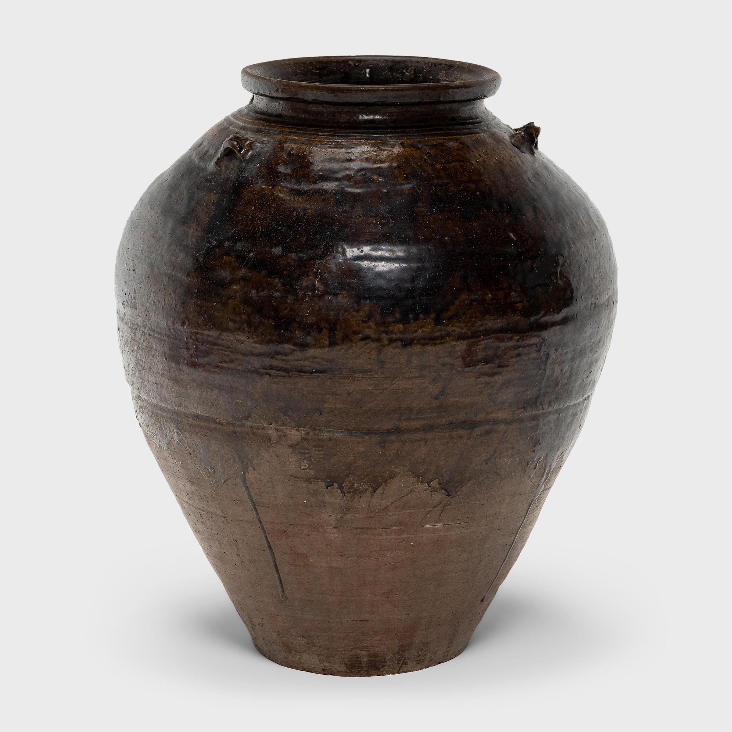 This large, glazed stoneware vessel is a Meiji-era Japanese storage jar (tsubo) used for storing rice wine, water or even tea leaves and spices. Sometimes referred to as a Martaban jar due to historic trade routes, this style of unrefined, ovoid jar