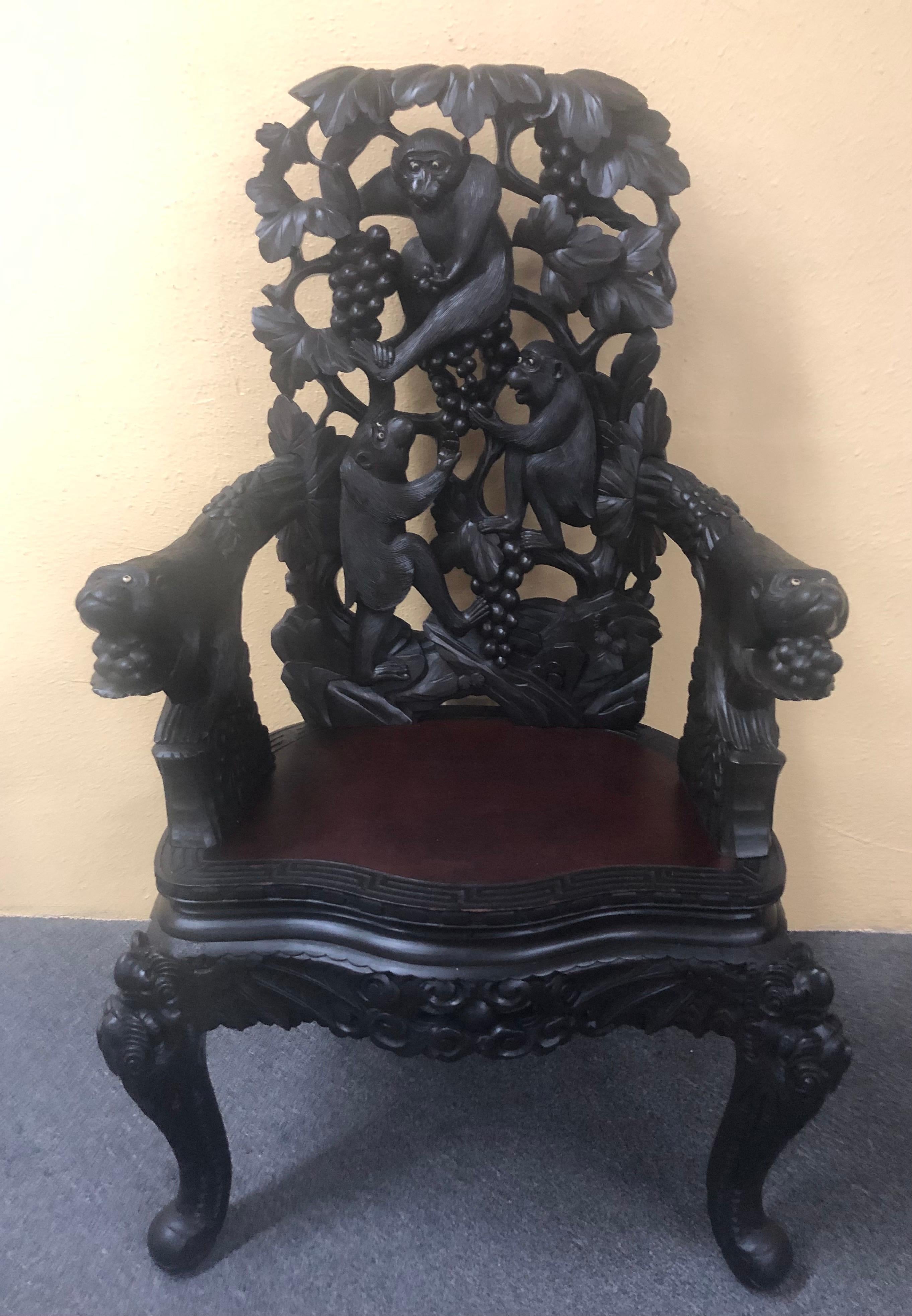Japanese hand carved dark wood export monkey armchair, circa 1940s. This antique Japanese armchair is intricately carved with the chair back depicting tree branches with monkeys. The chair has exceptional detail with monkey heads as arms with inlaid