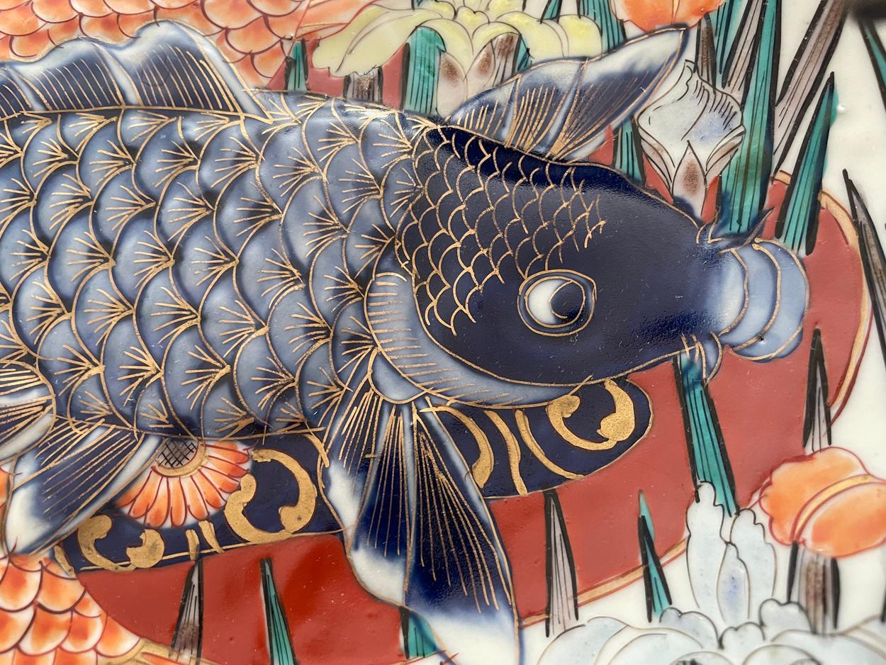 Magnifique plat ovale japonais Imari peint à la main, aux bords cannelés, abondamment décoré dans des tons vibrants de bleu, rouge, orange, vert et jaune, avec des superpositions dorées, représentant deux grandes carpes Koï dans des tons vibrants