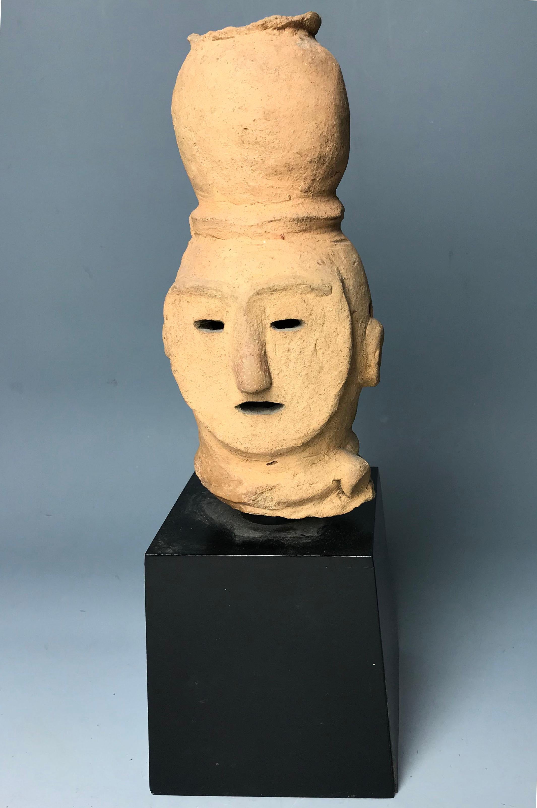 A rare Haniwa figural head 
Kofun period (3rd-7th century), circa 500-600.
The hand-built yellow earthenware hollow figure of typical form, the face highlighted by three slit type openings for the eyes and mouth, the nose forehead and ears simply