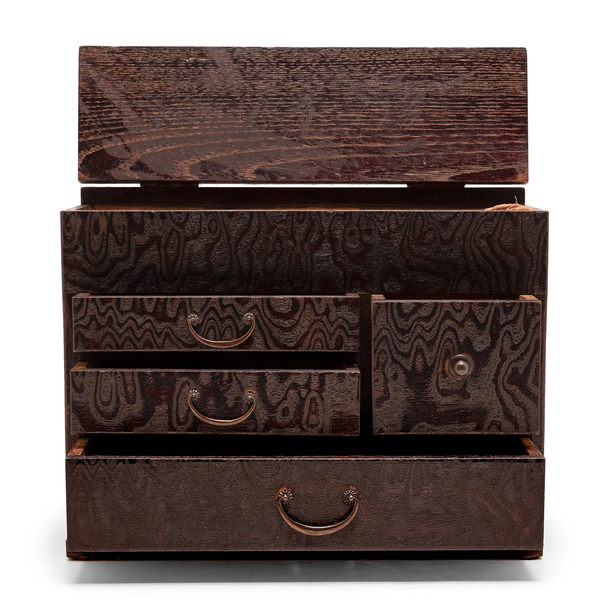 This elegant box with many drawers is a Japanese haribako, a tabletop chest used for storing sewing supplies, jewelry, or other accessories. The small chest features four drawers and a lid that lifts to reveal a shallow compartment and a removable